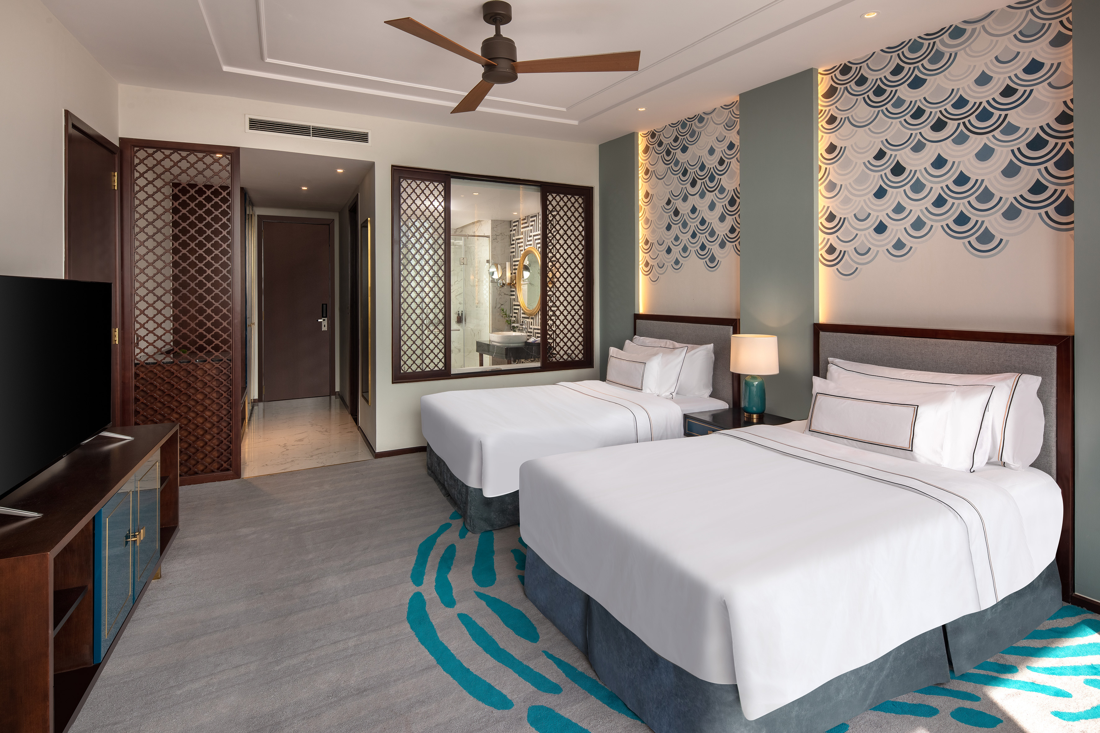 Modern hotel room with twin beds, blue wave wall decor, and ceiling fan.