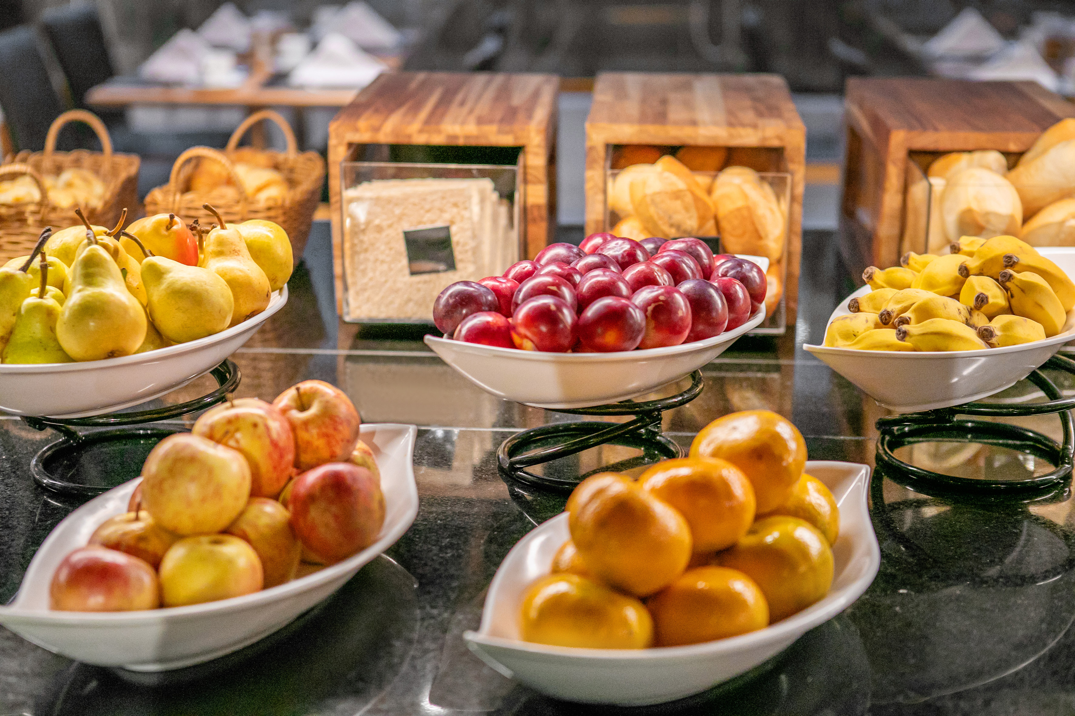 Fresh fruit buffet with pears, plums, bananas, apples, oranges, and bread rolls.