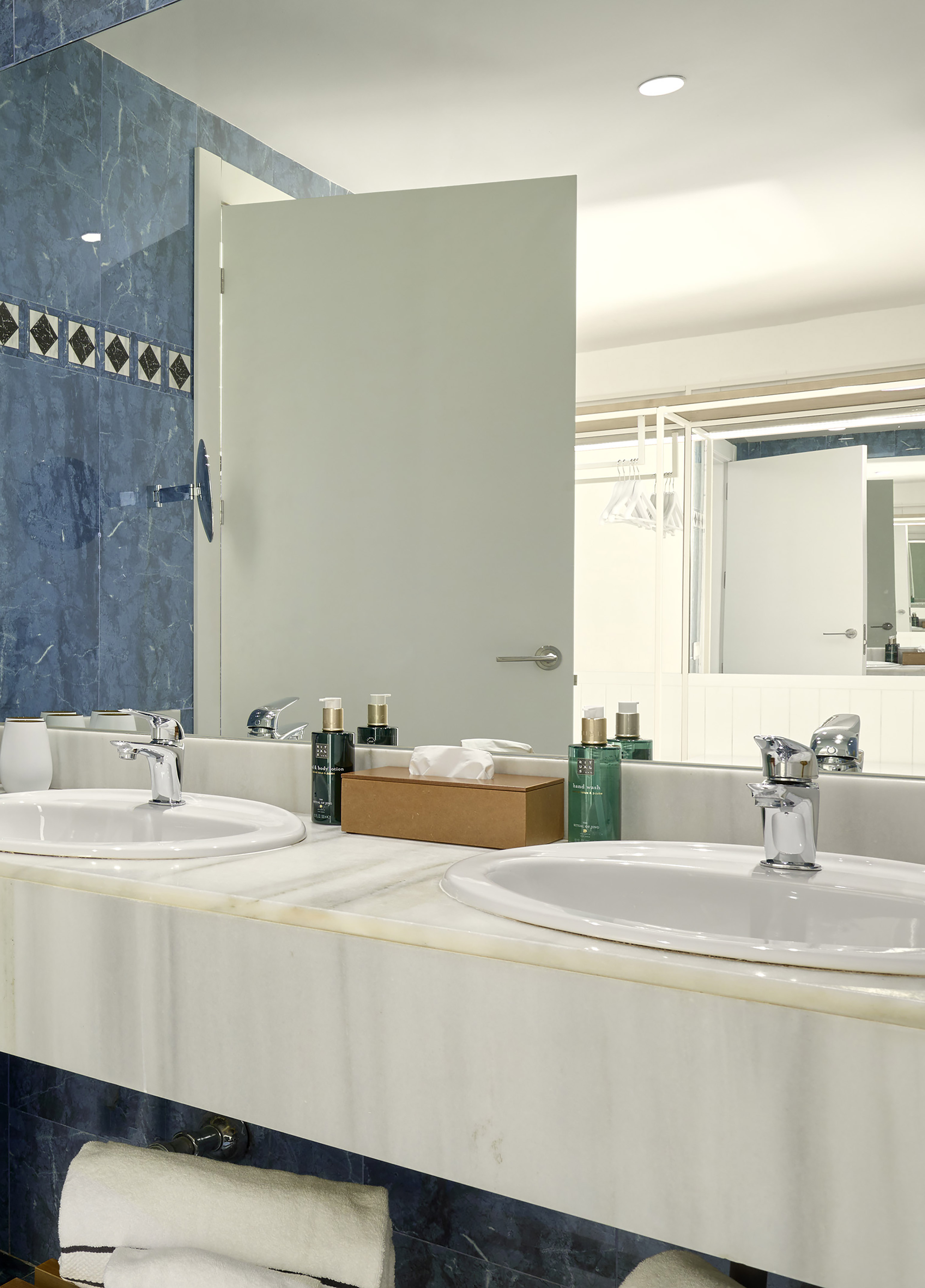 Bathroom with dual sinks, marble vanity, blue tiled wall, and toiletries.
