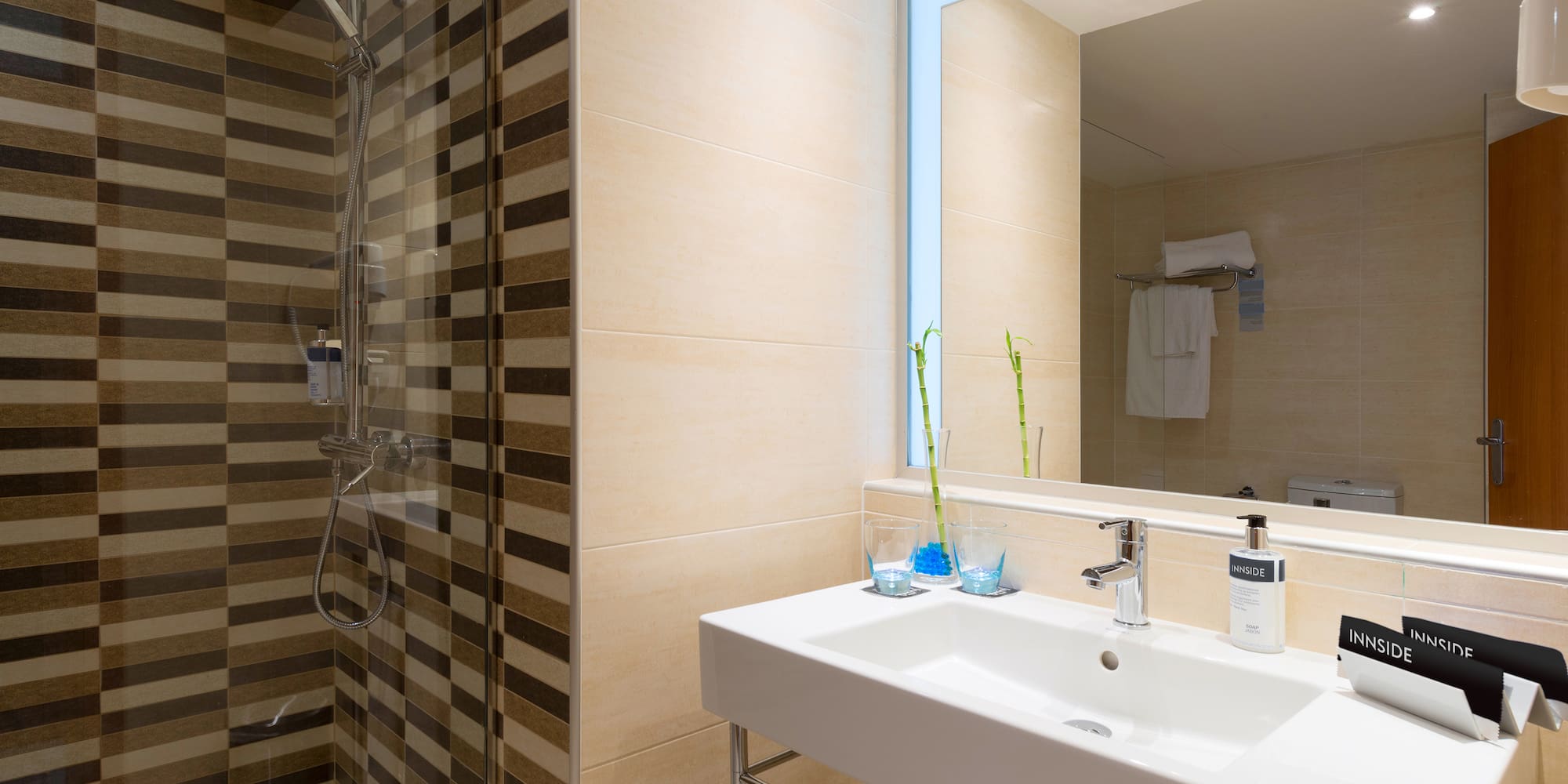 Modern hotel bathroom with striped shower, white sink, mirror, and Innside amenities.