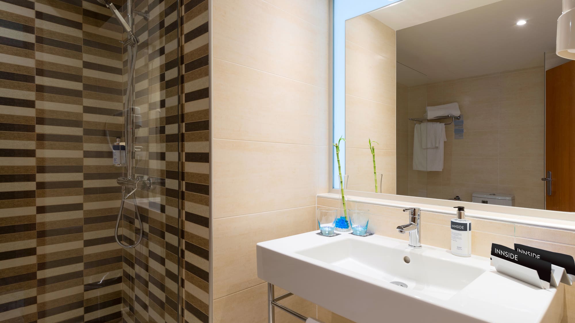 Modern hotel bathroom with striped shower, white sink, mirror, and Innside amenities.