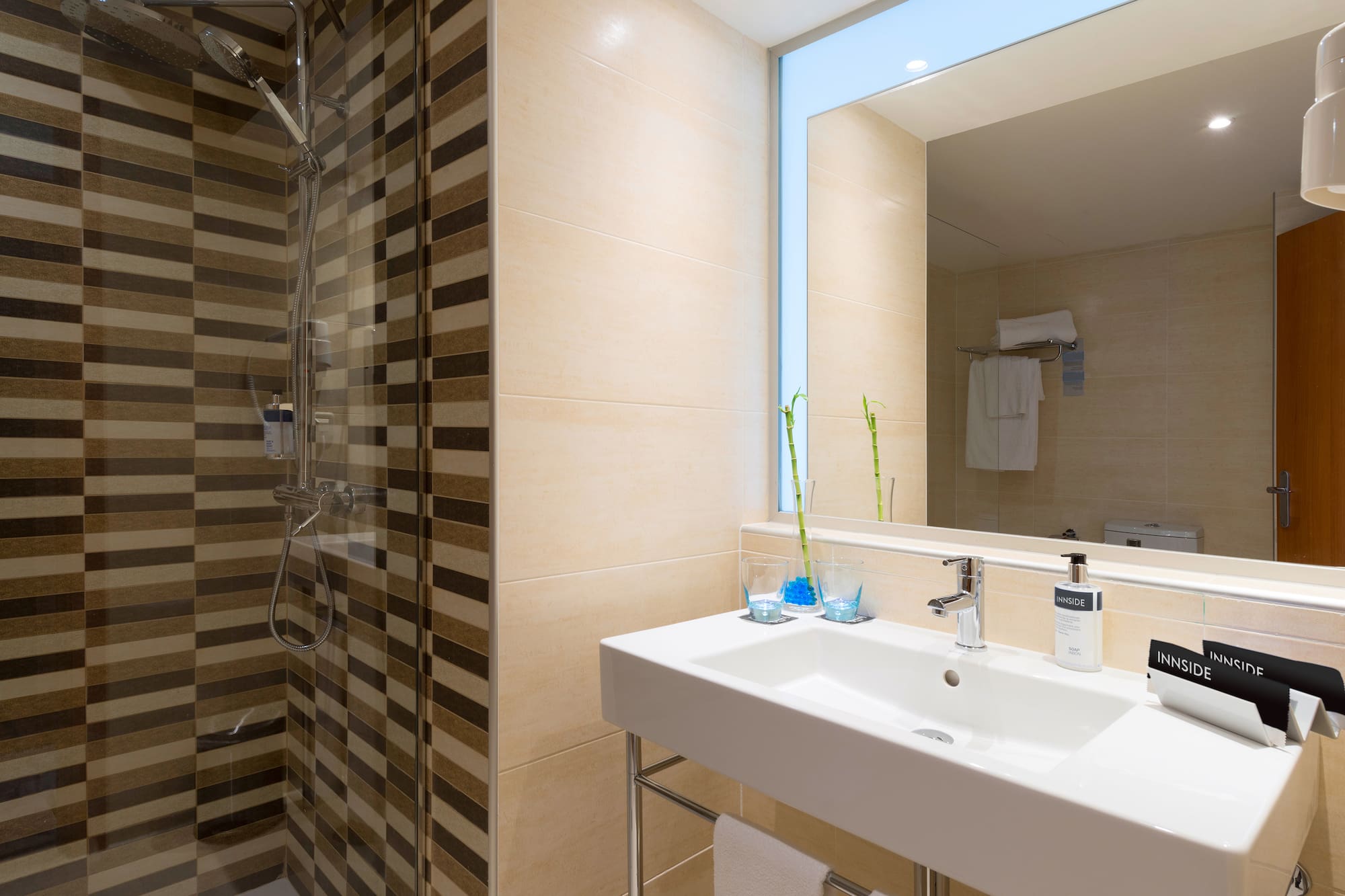 Modern hotel bathroom with striped shower, white sink, mirror, and Innside amenities.