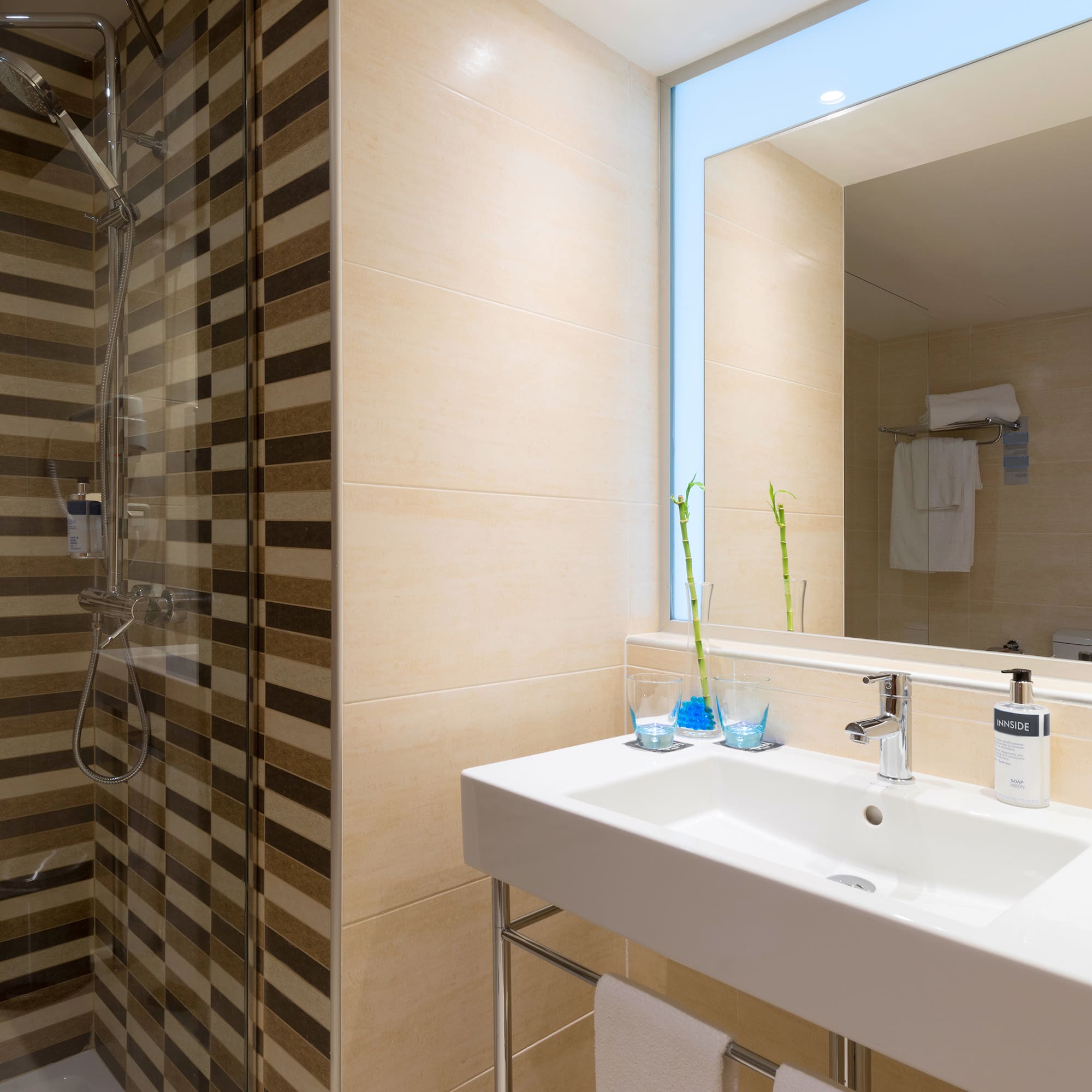 Modern hotel bathroom with striped shower, white sink, mirror, and Innside amenities.