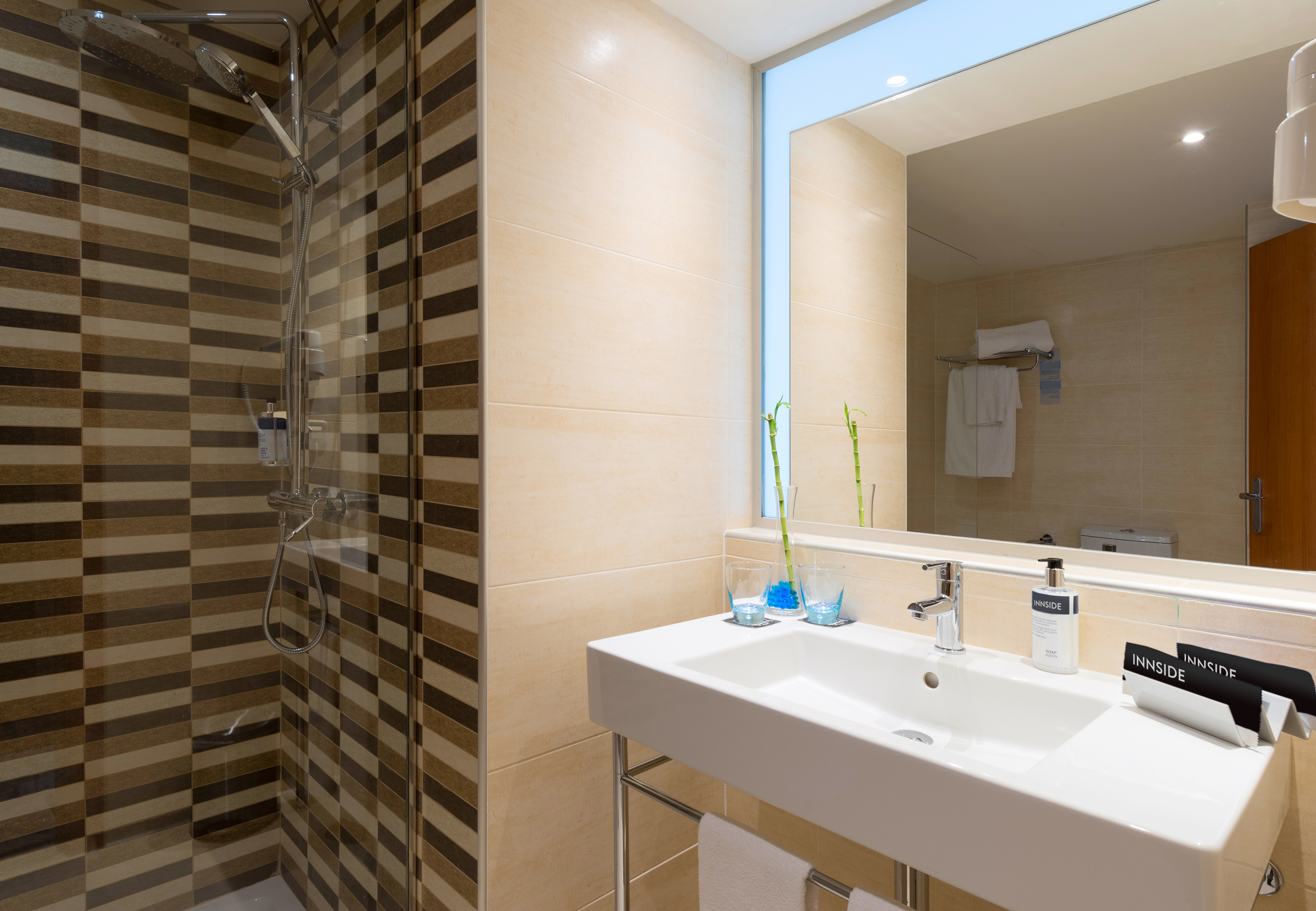 Modern hotel bathroom with striped shower, white sink, mirror, and Innside amenities.
