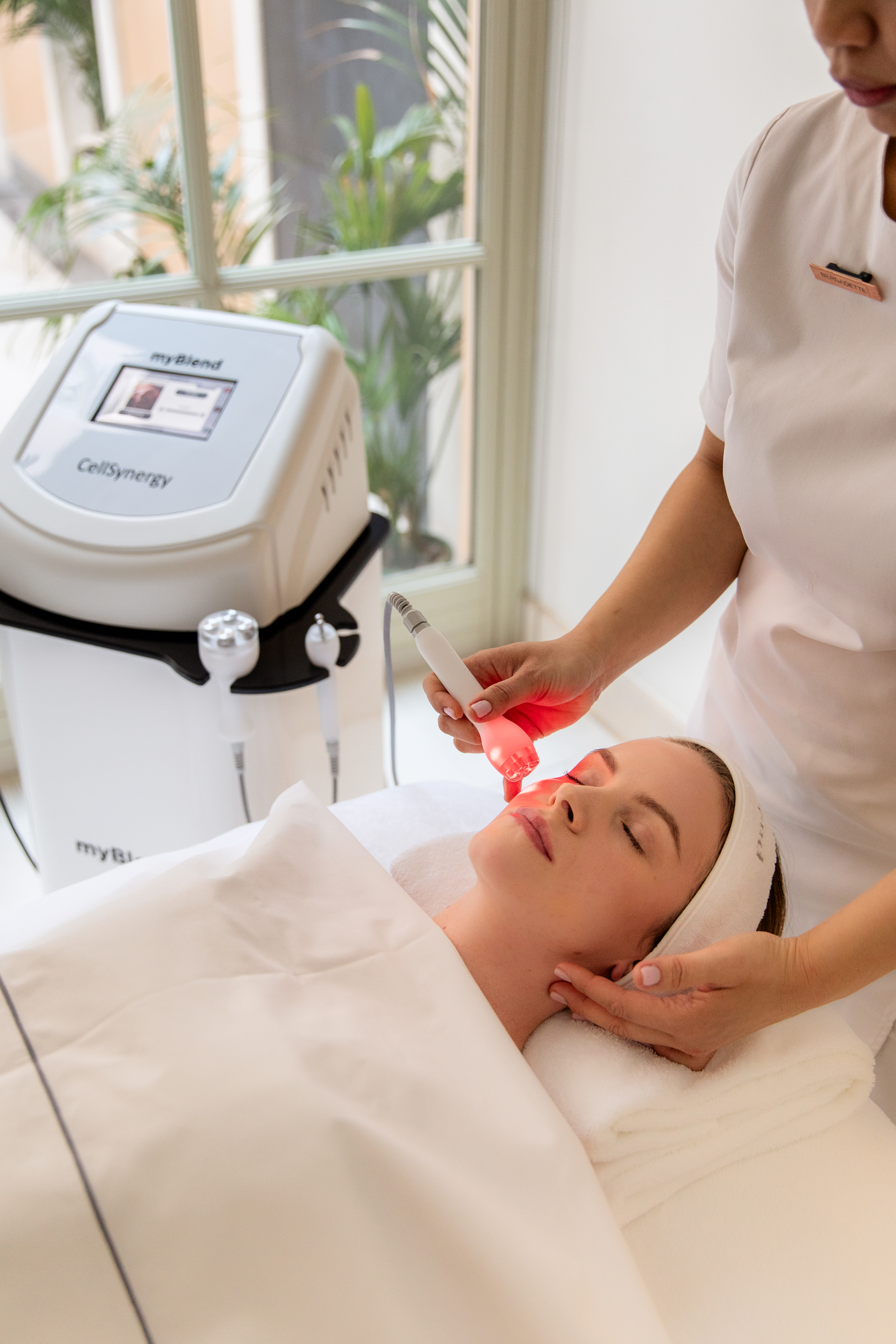 Woman receiving red LED light therapy facial with myBlend CellSynergy machine.