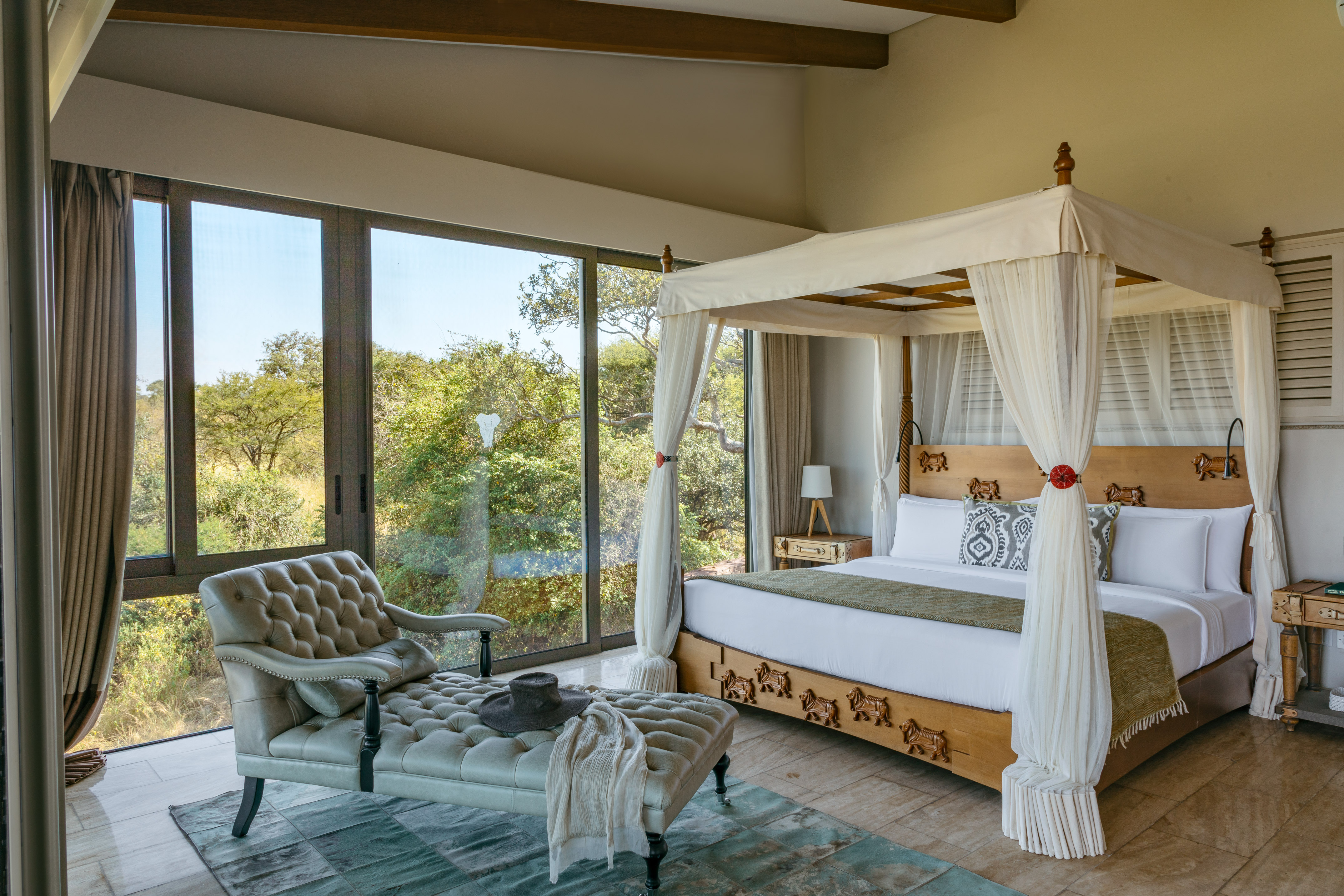 Luxury safari lodge bedroom with four-poster bed and panoramic nature view.