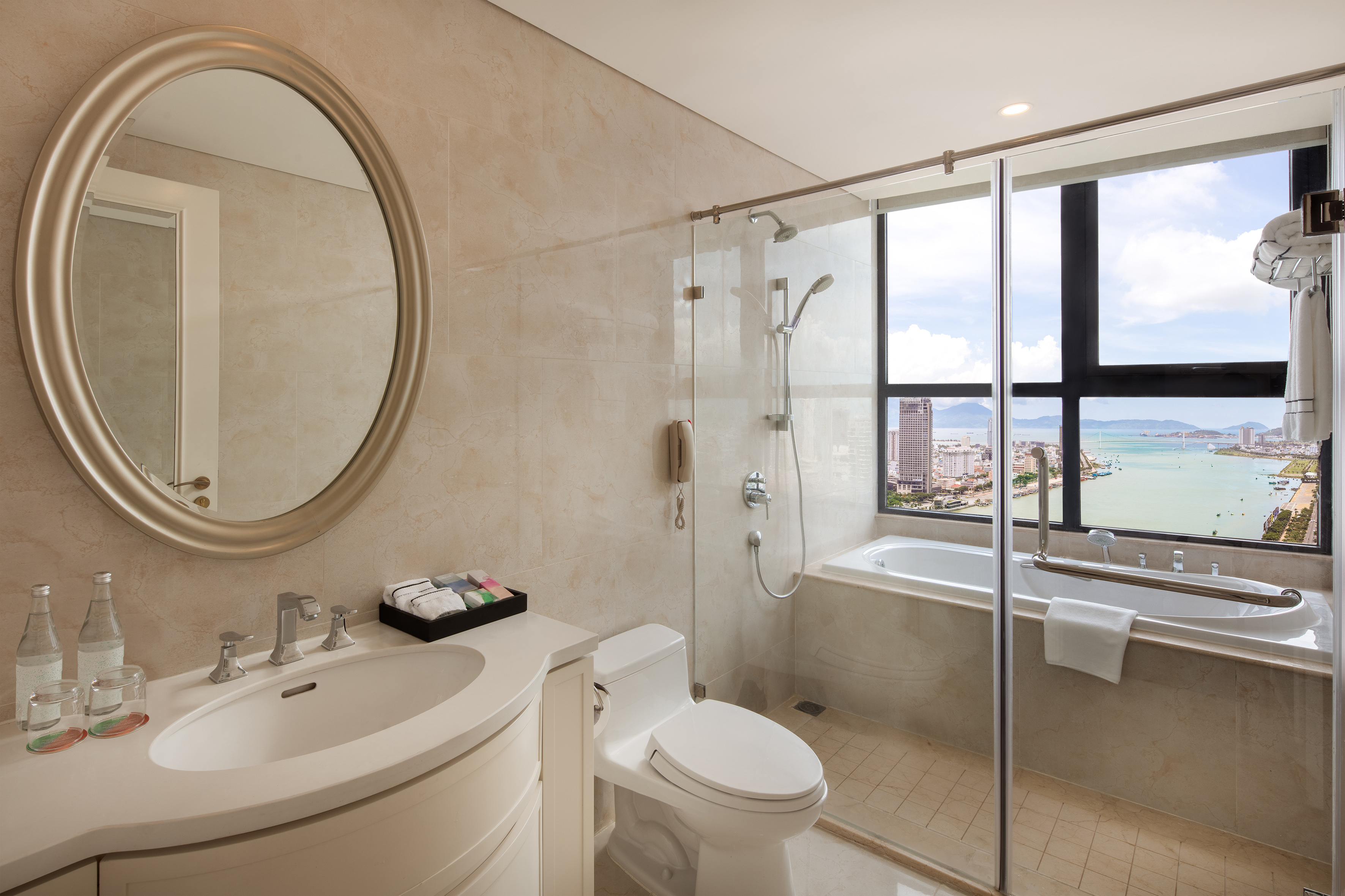 Modern hotel bathroom with city and ocean view, bathtub, shower, vanity.