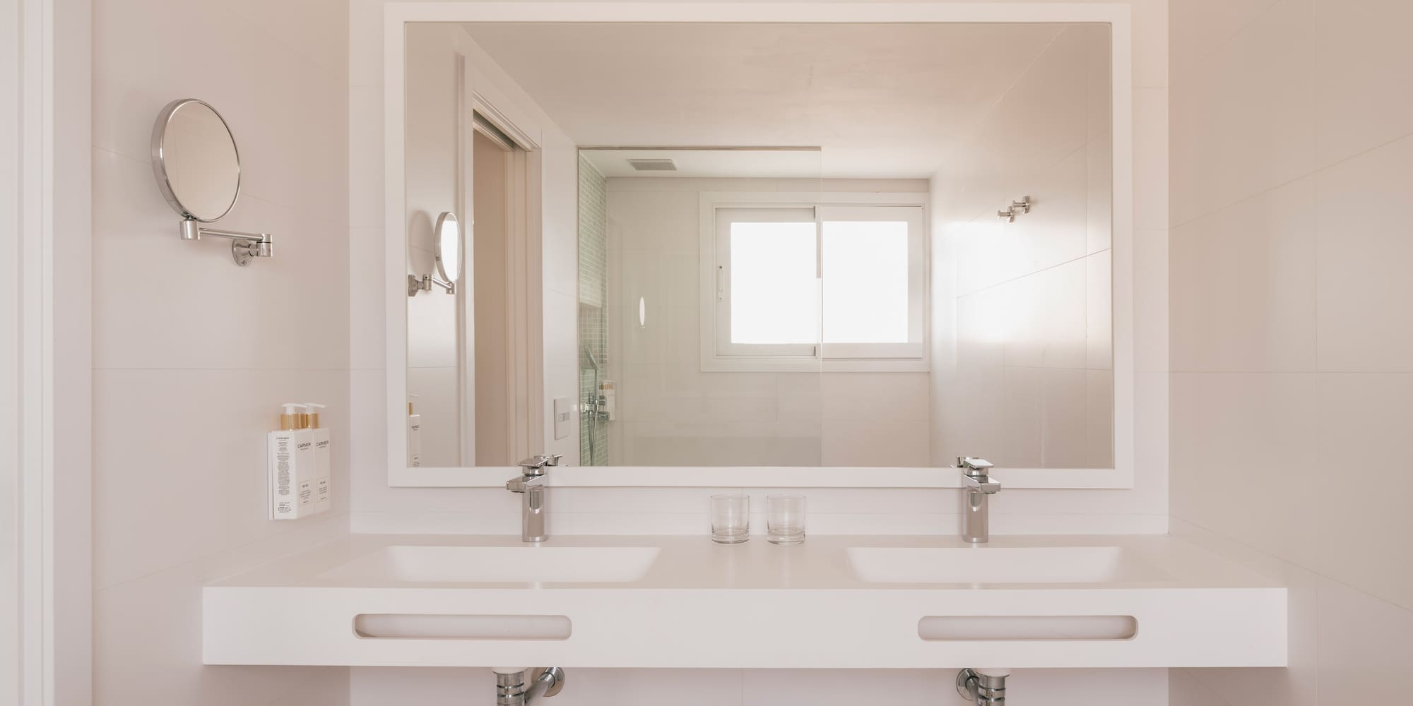 Modern bathroom with double vanity, large mirror reflecting shower and window.
