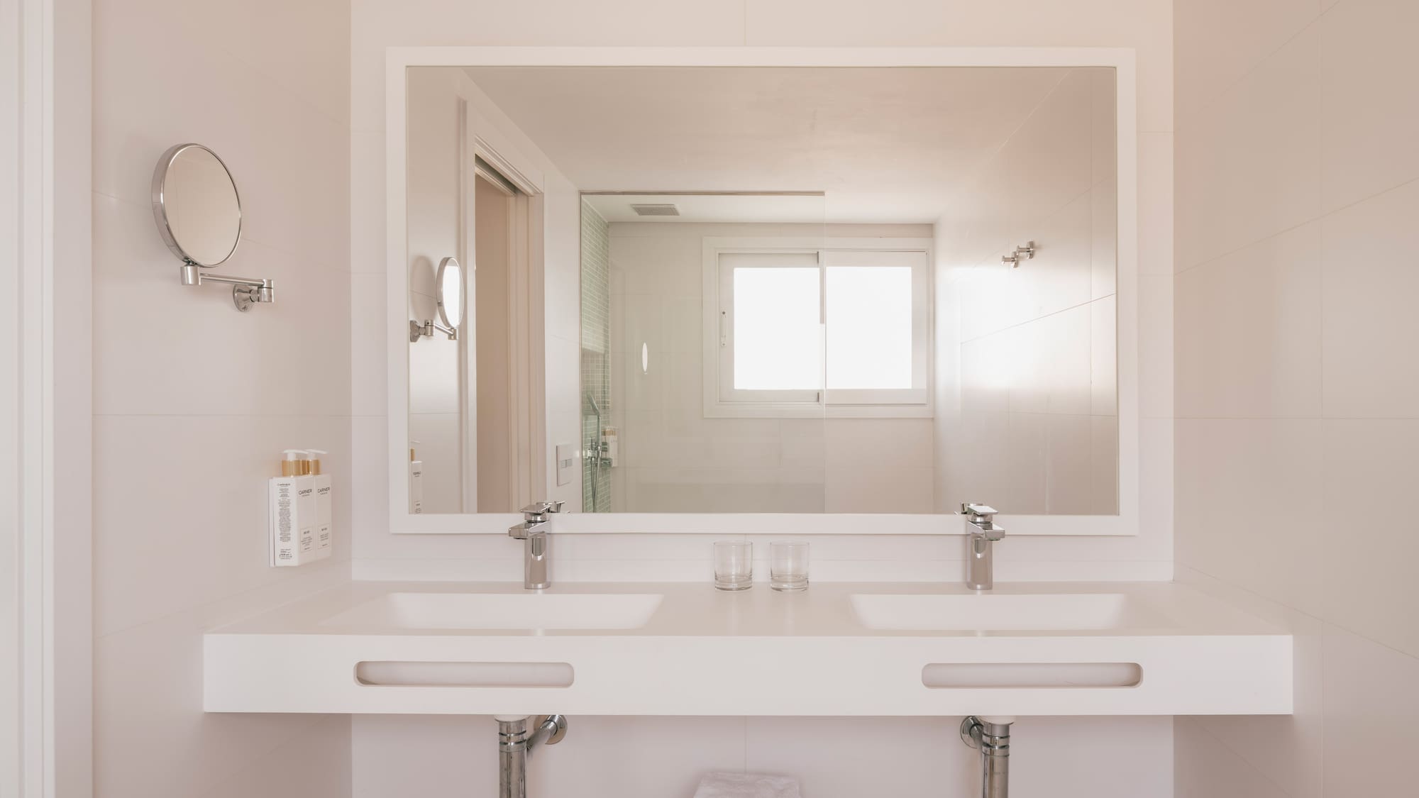 Modern bathroom with double vanity, large mirror reflecting shower and window.