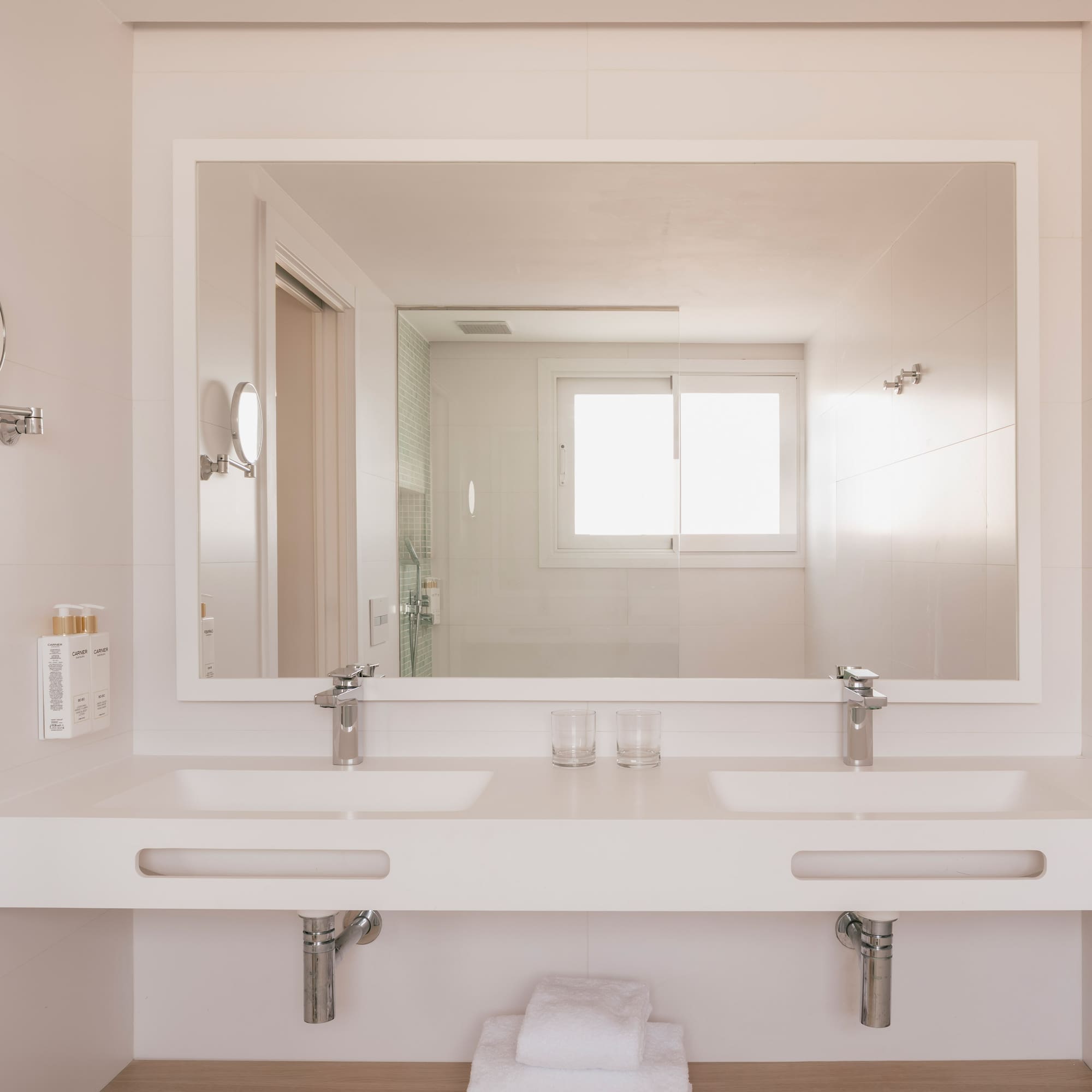 Modern bathroom with double vanity, large mirror reflecting shower and window.