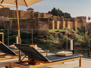 Luxury resort terrace with lounge chairs overlooking Málaga's Alcazaba fortress.