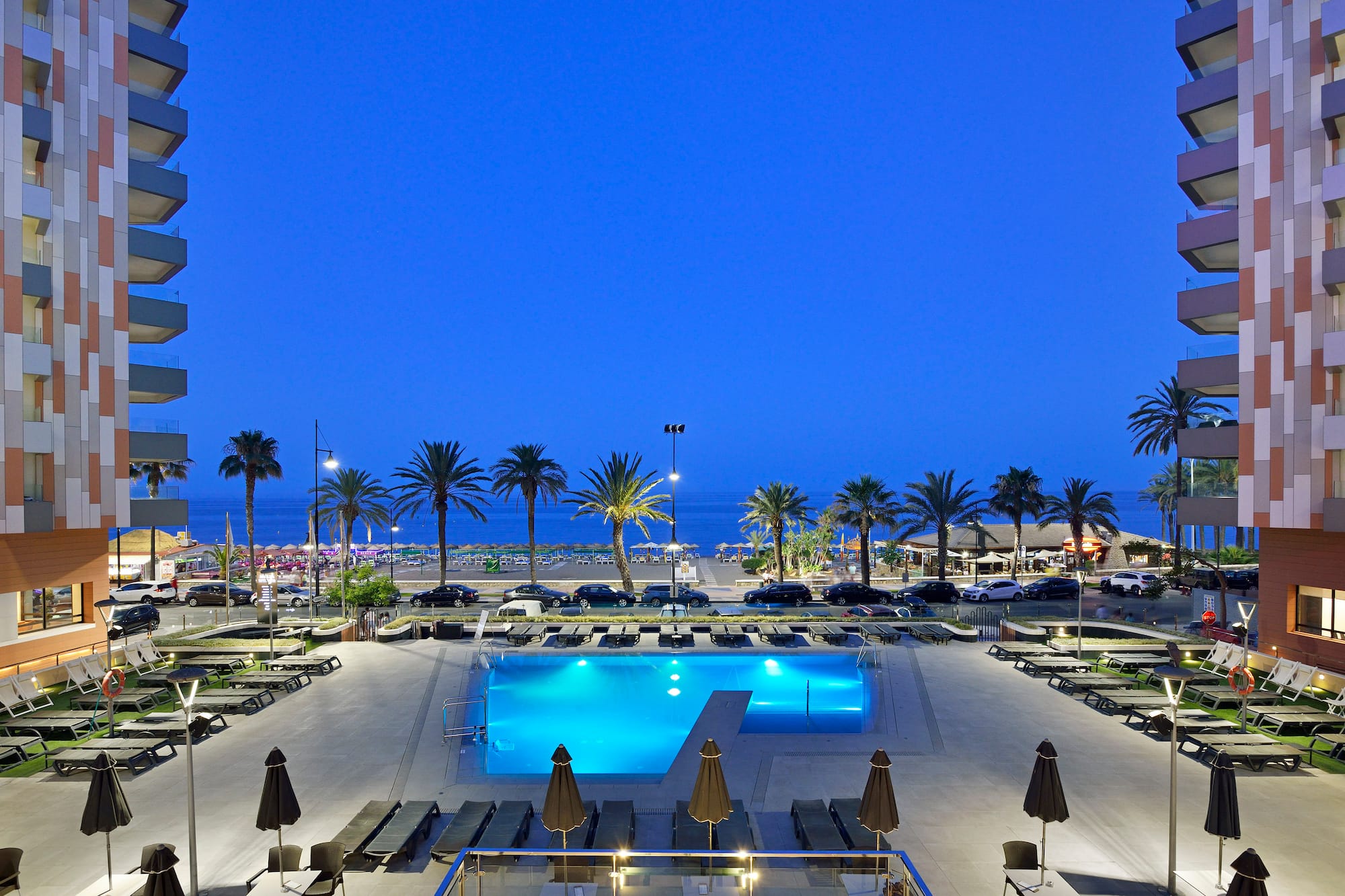 Hotel swimming pool illuminated at night, with beach, ocean, and palm trees.