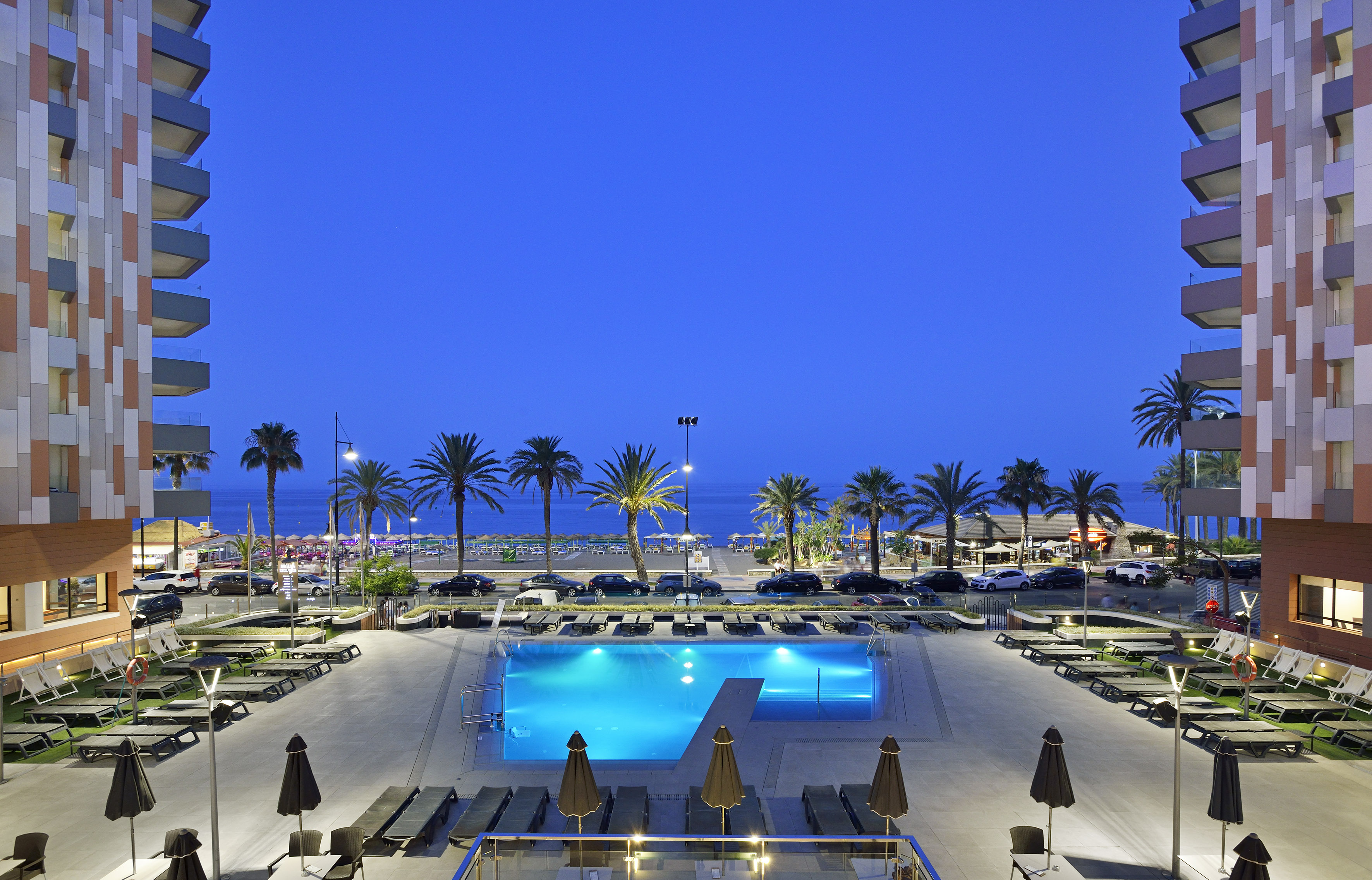 Hotel swimming pool illuminated at night, with beach, ocean, and palm trees.