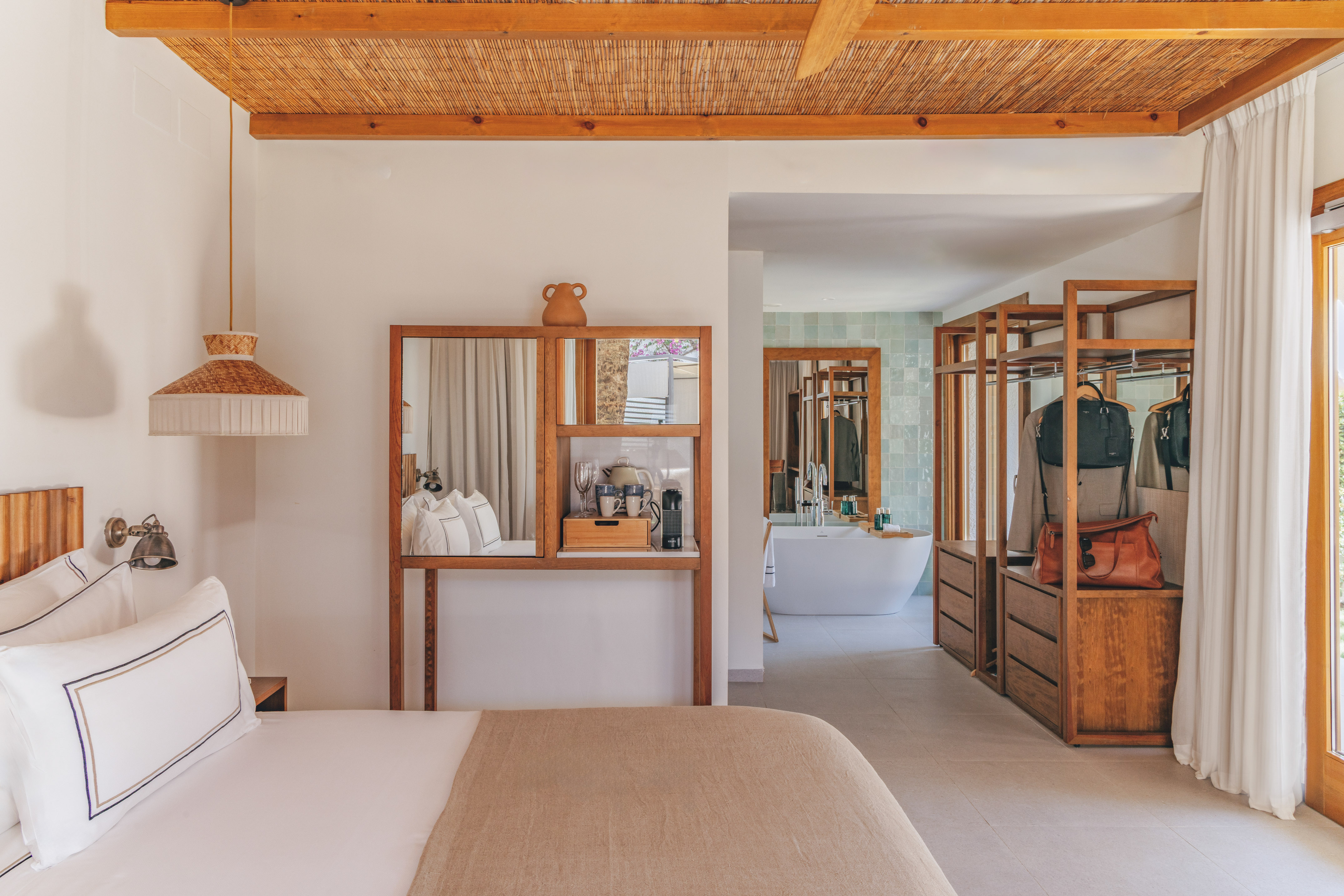 Modern hotel bedroom with open wood closet, bamboo ceiling, and bathroom.