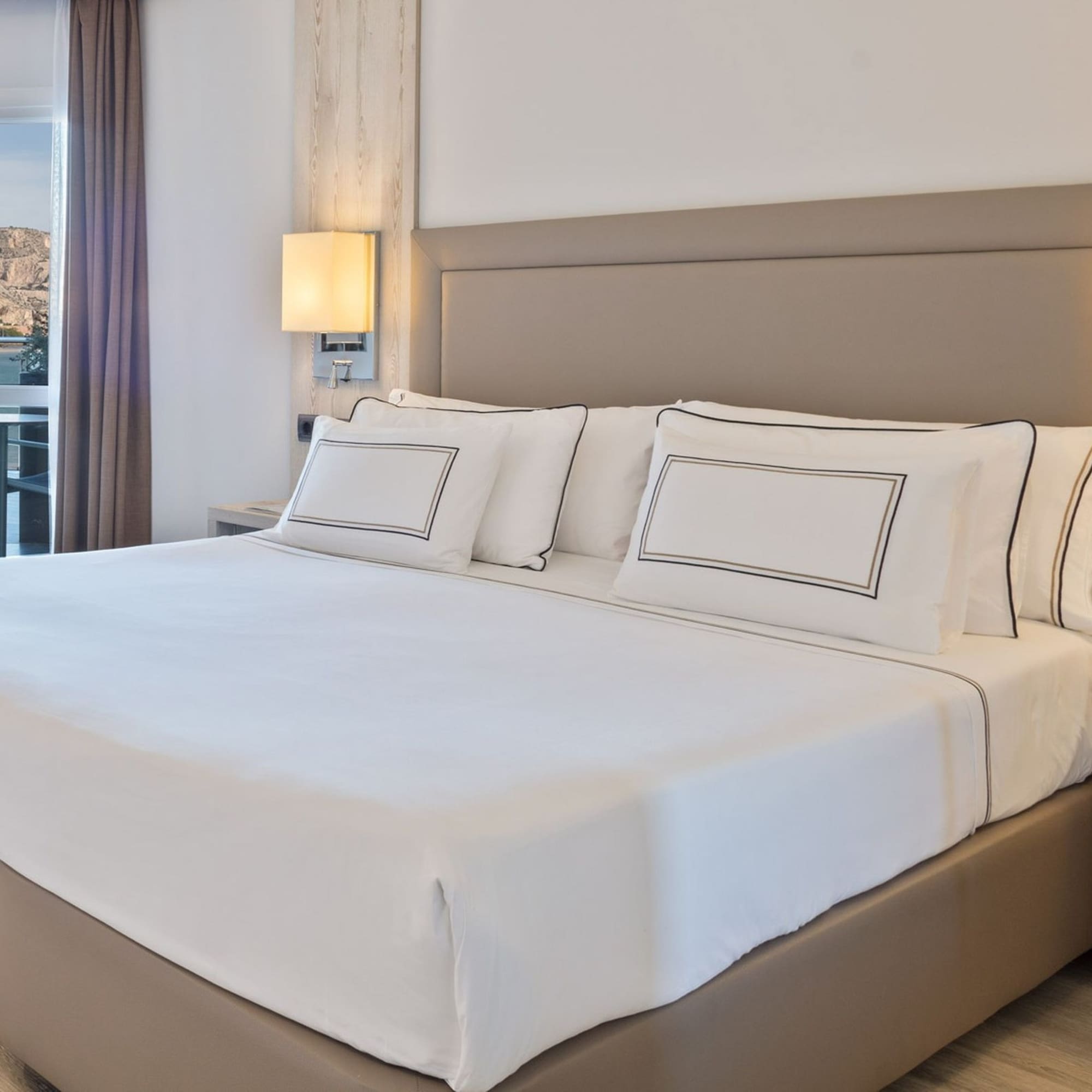 Habitación de hotel moderna con cama doble, vista al mar y montaña desde balcón.