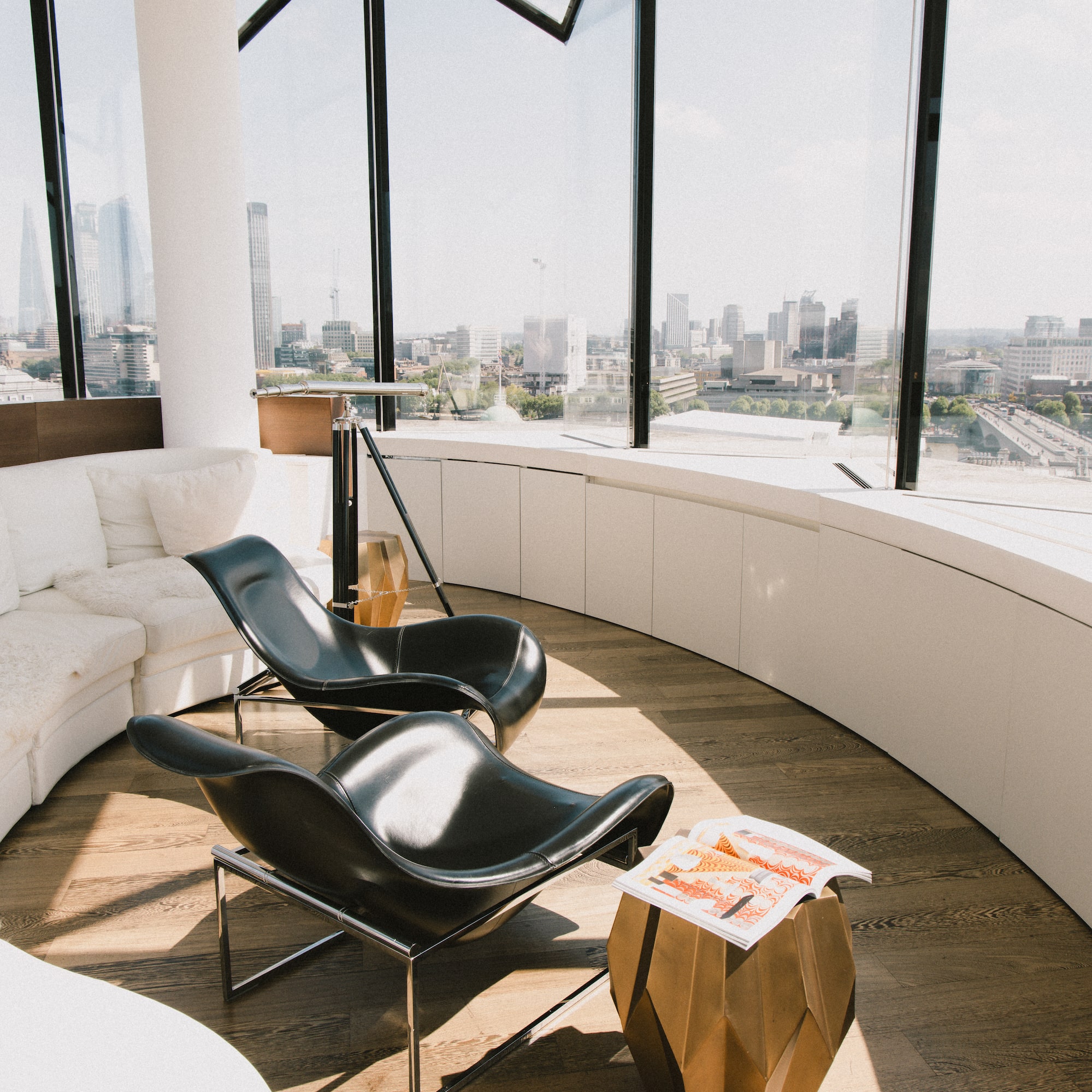 Modern lounge with city skyline, curved white sofa, black lounge chairs.