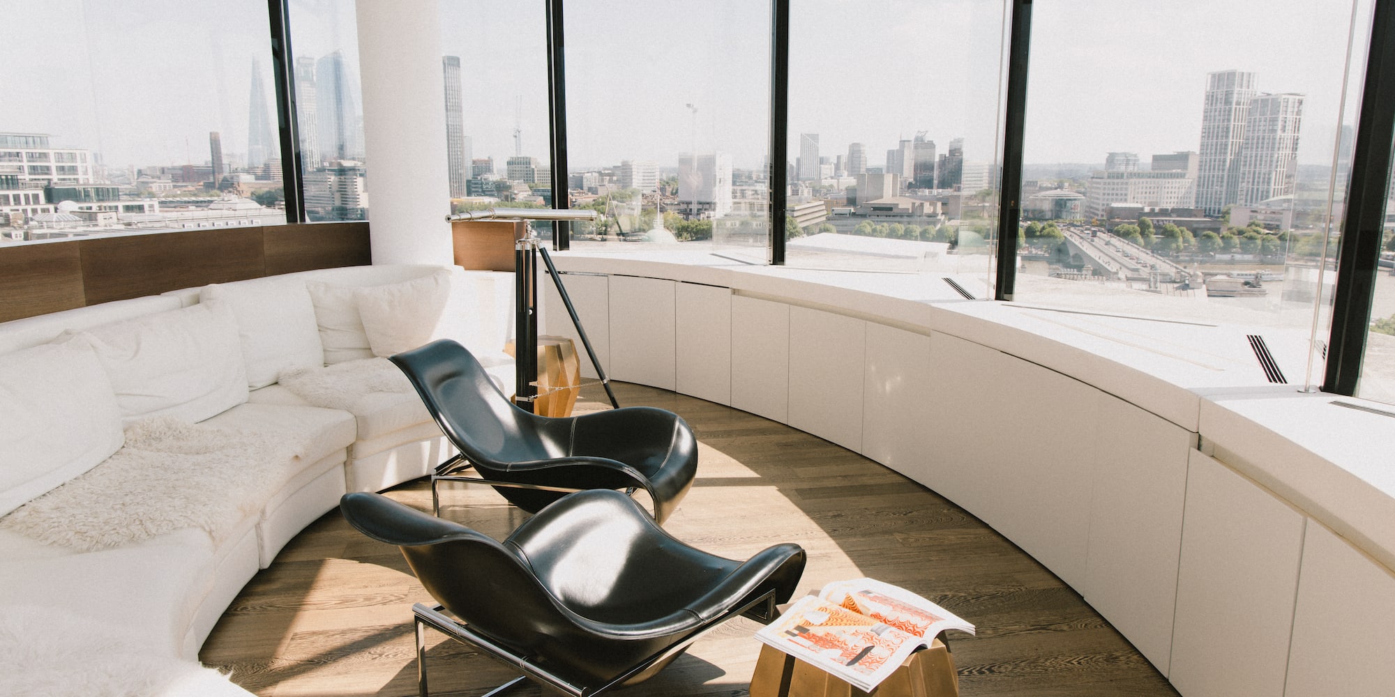 Modern lounge with city skyline, curved white sofa, black lounge chairs.
