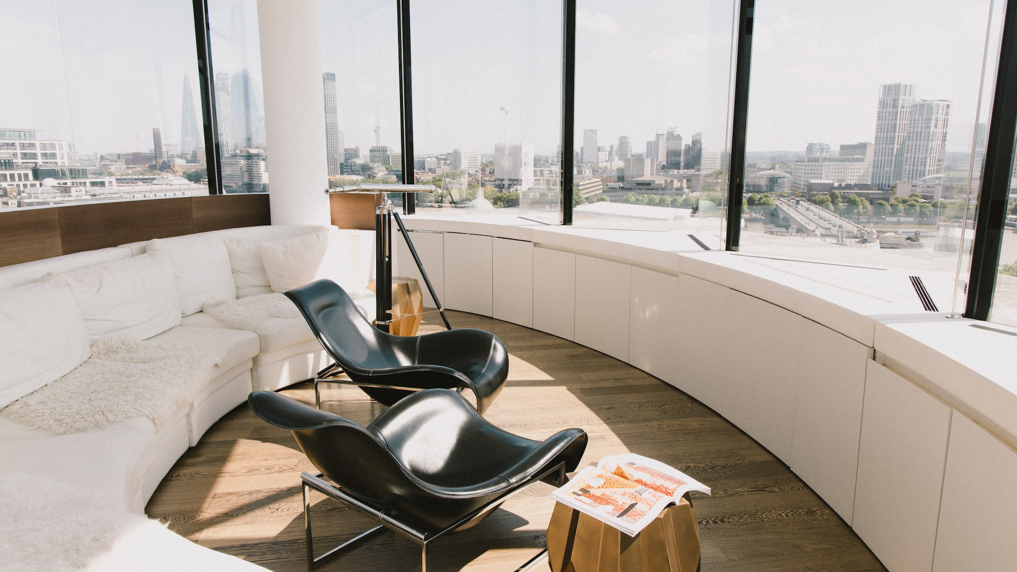Modern lounge with city skyline, curved white sofa, black lounge chairs.