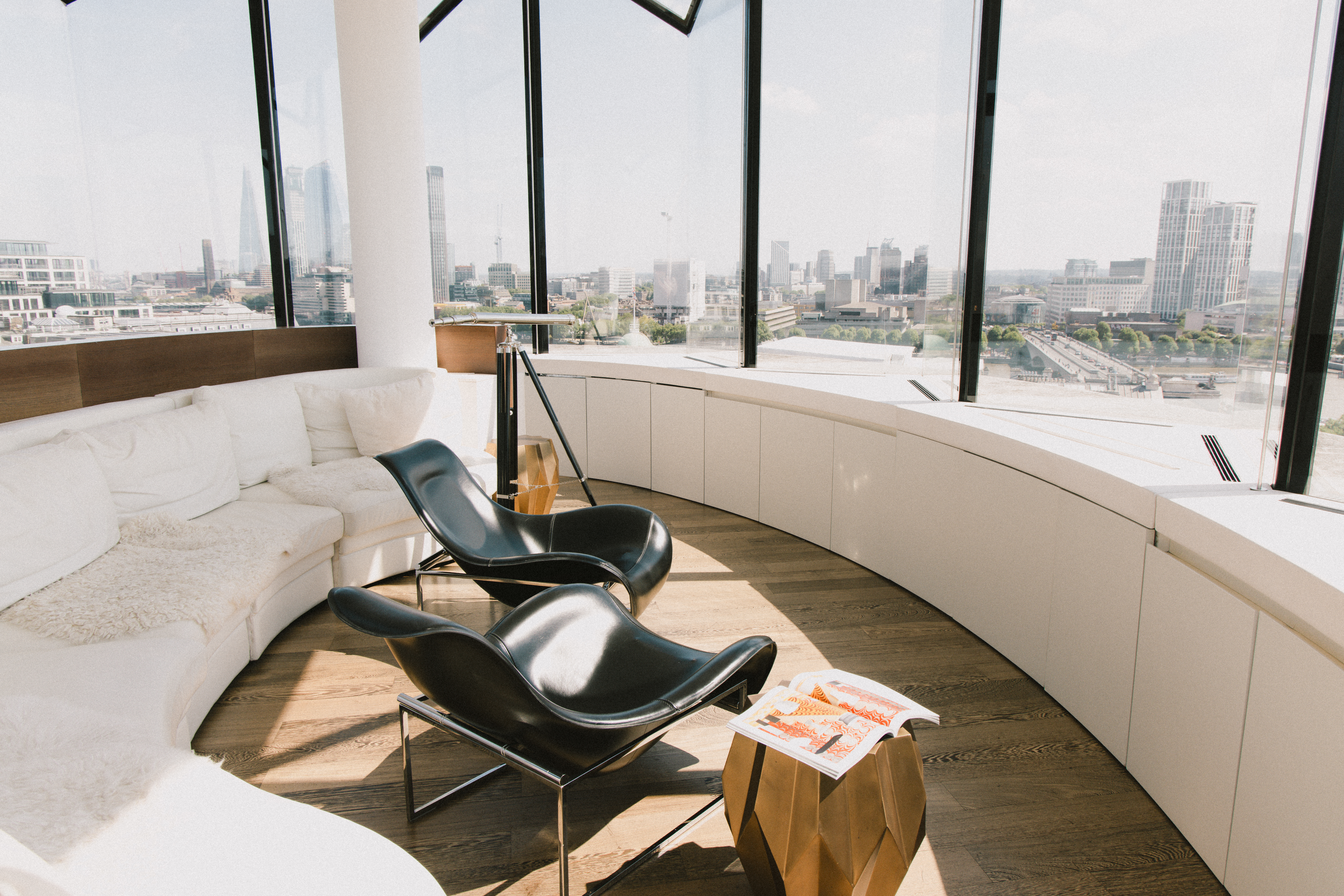 Modern lounge with city skyline, curved white sofa, black lounge chairs.