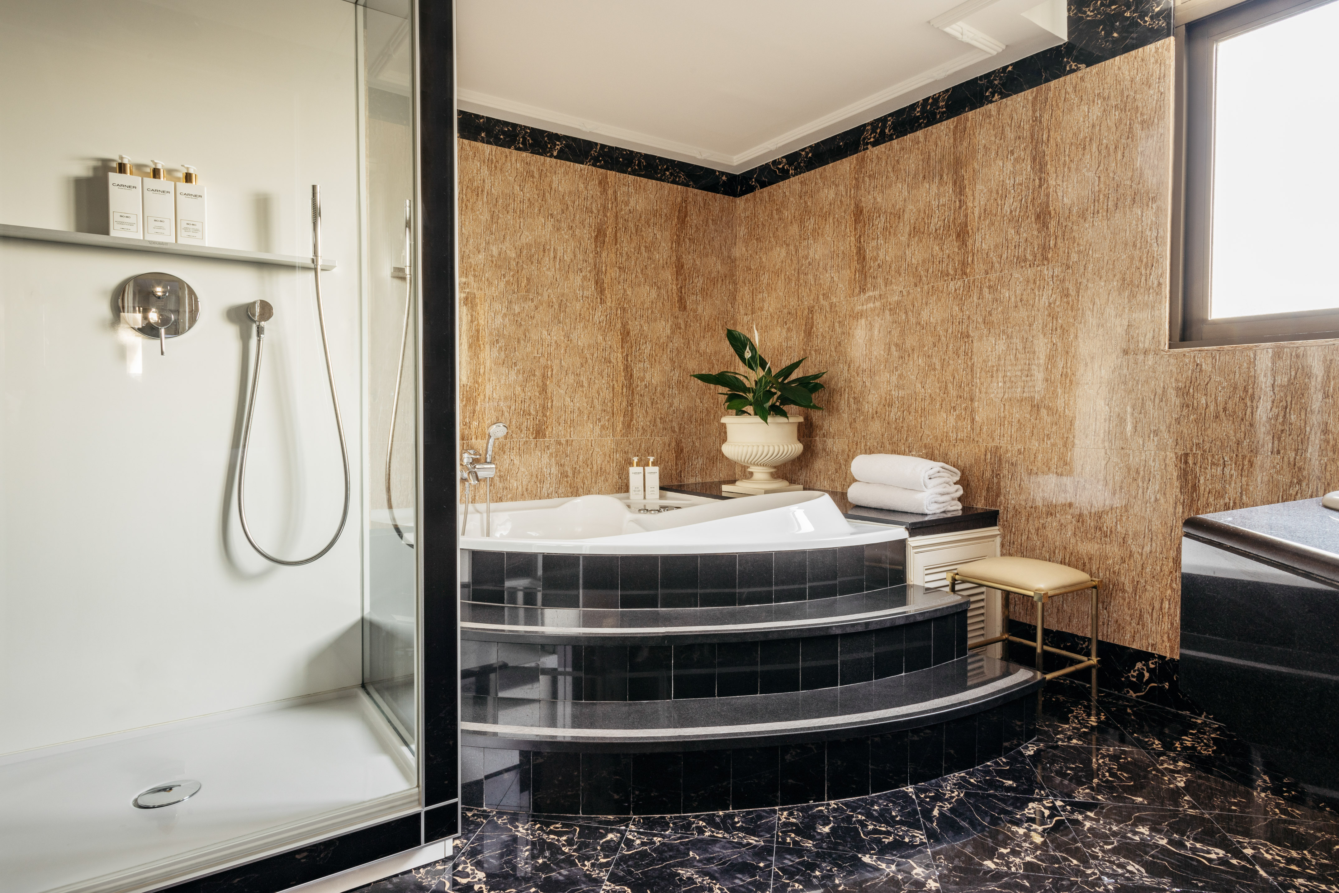 Elegant bathroom: jetted tub, glass shower, black marble floor, and textured walls.