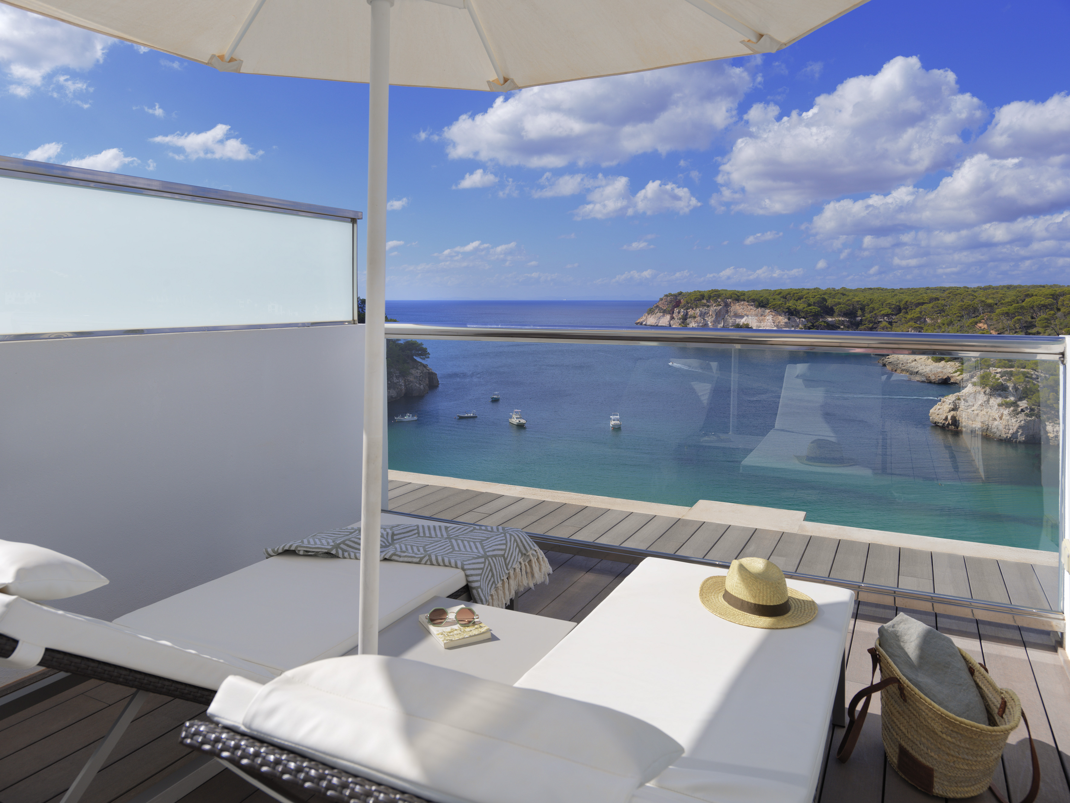 Hotel balcony with sun loungers, umbrella, and stunning Mediterranean sea view.