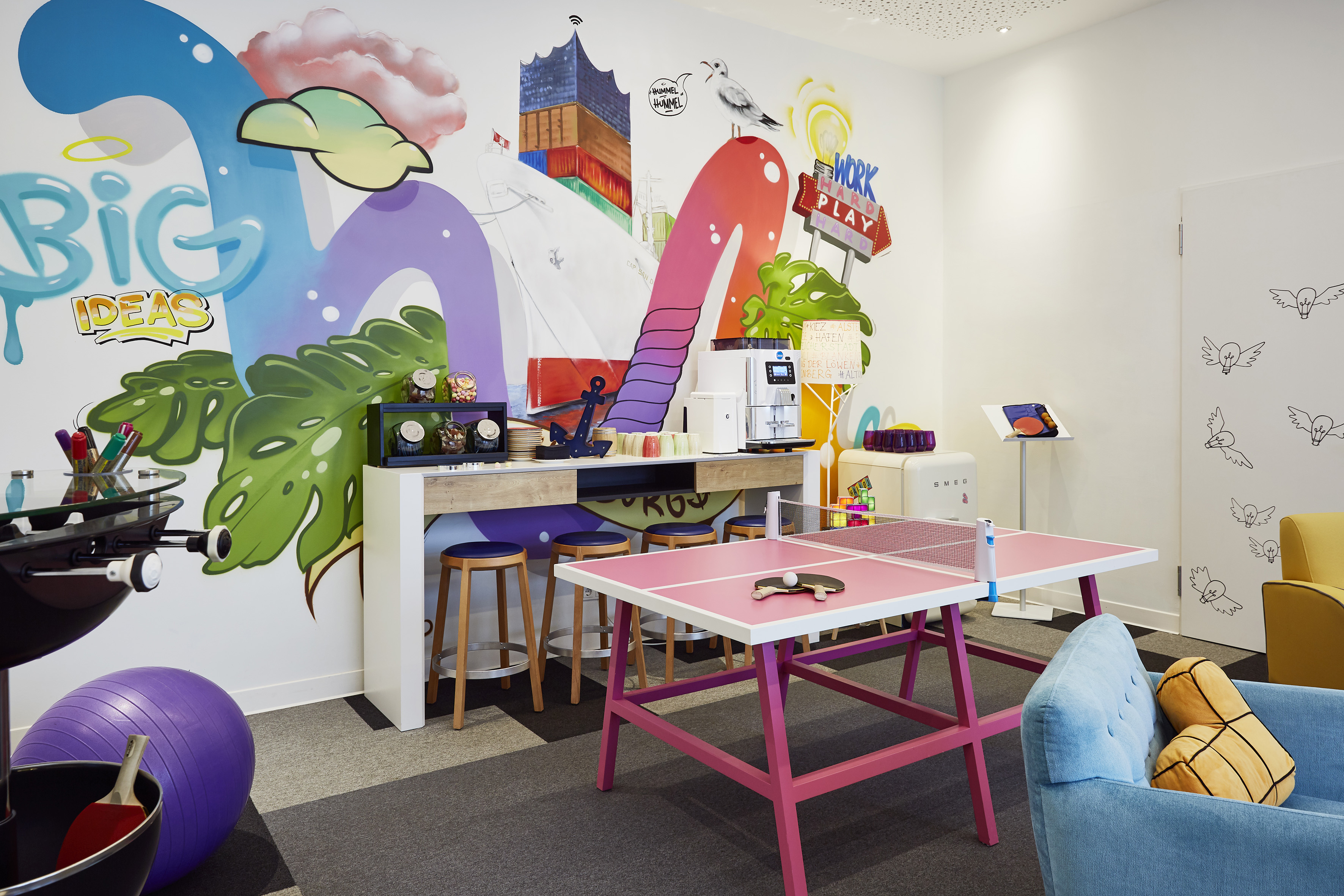 Creative office breakroom with pink ping pong table, "Big Ideas" mural, and coffee bar.