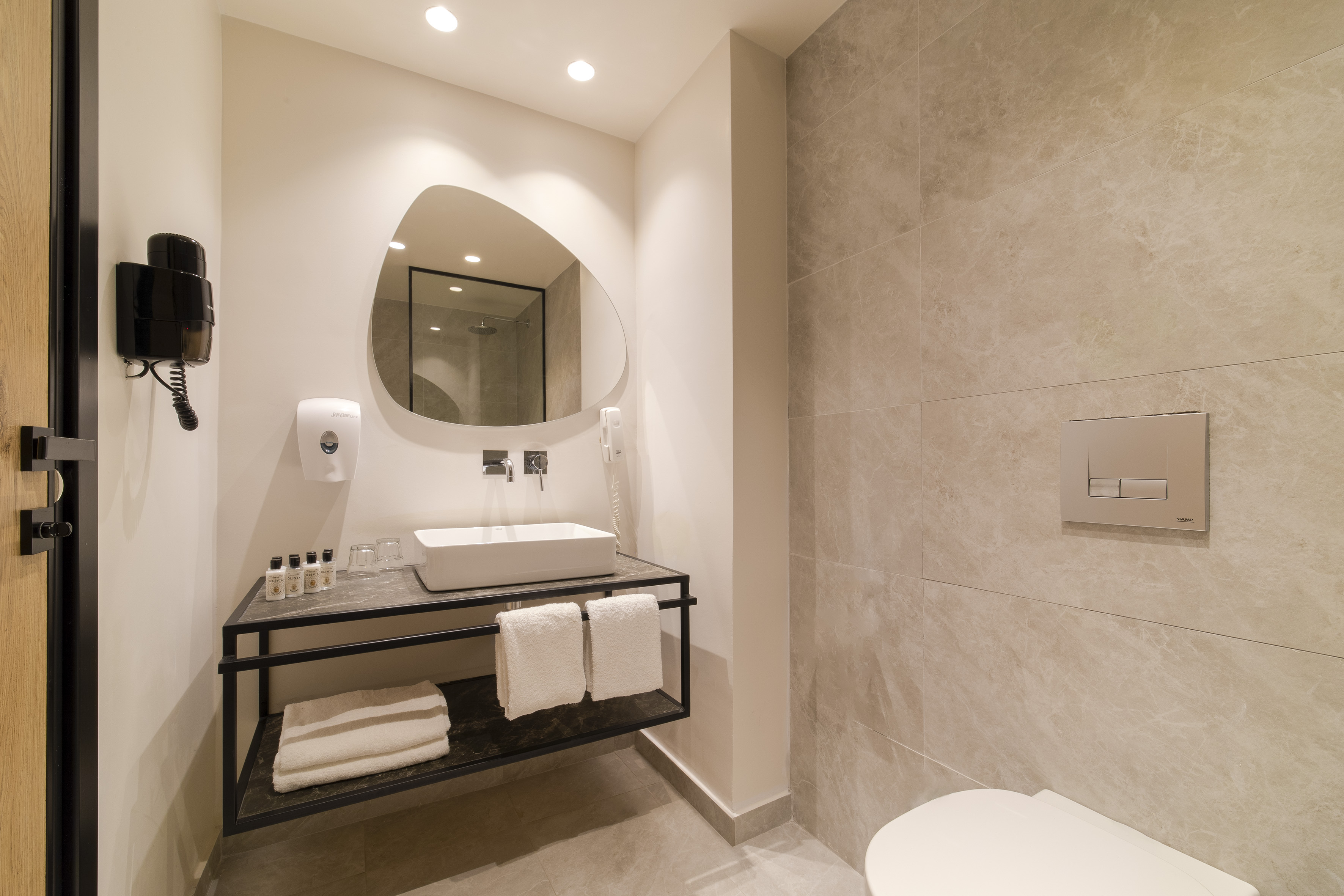 Contemporary hotel bathroom with white sink, organic mirror, and tiled walls.