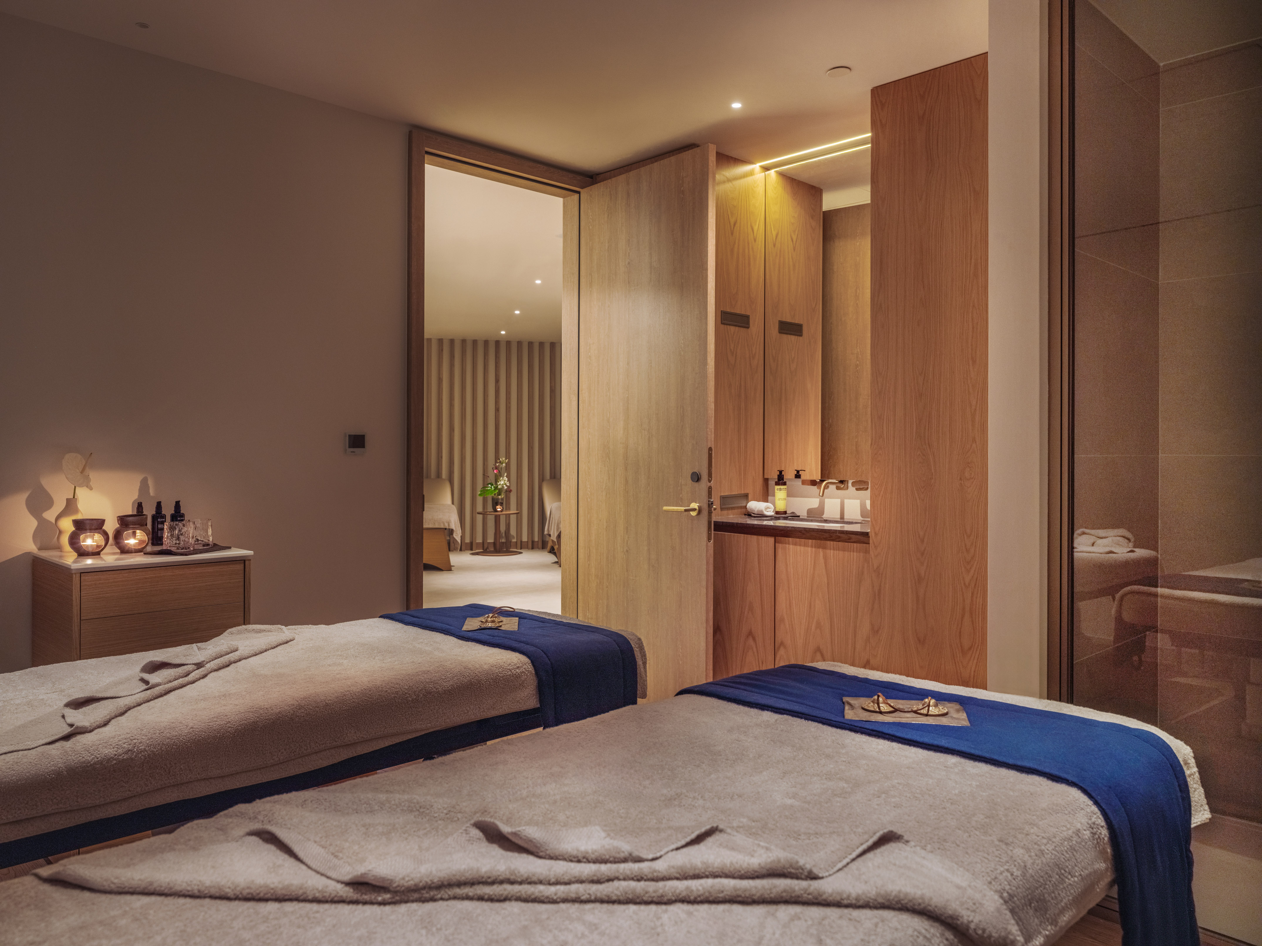 Relaxing spa massage room with two treatment beds, warm lighting, and wood accents.