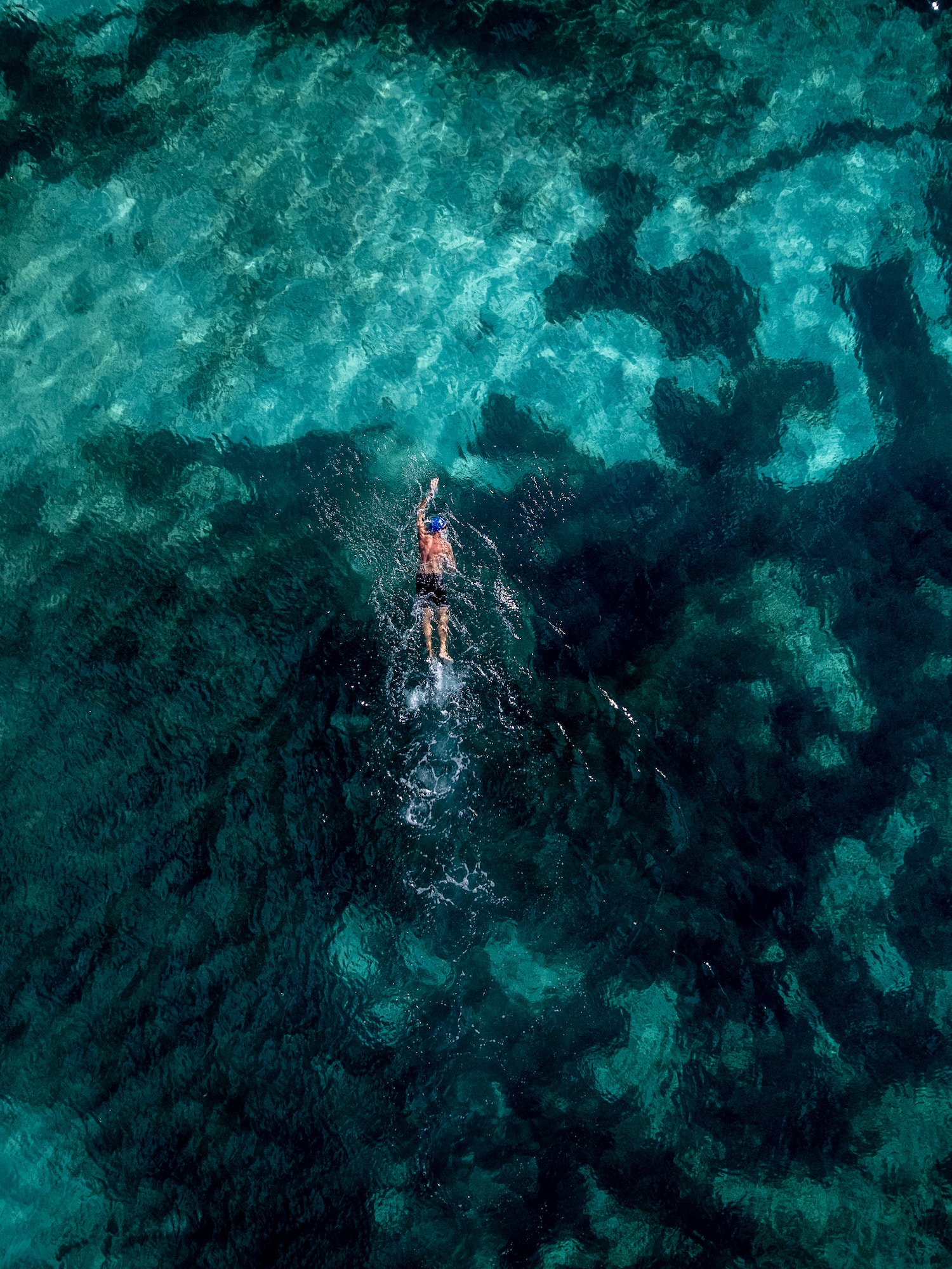 Nadador en aguas turquesas del océano, vista aérea de fondo marino.
