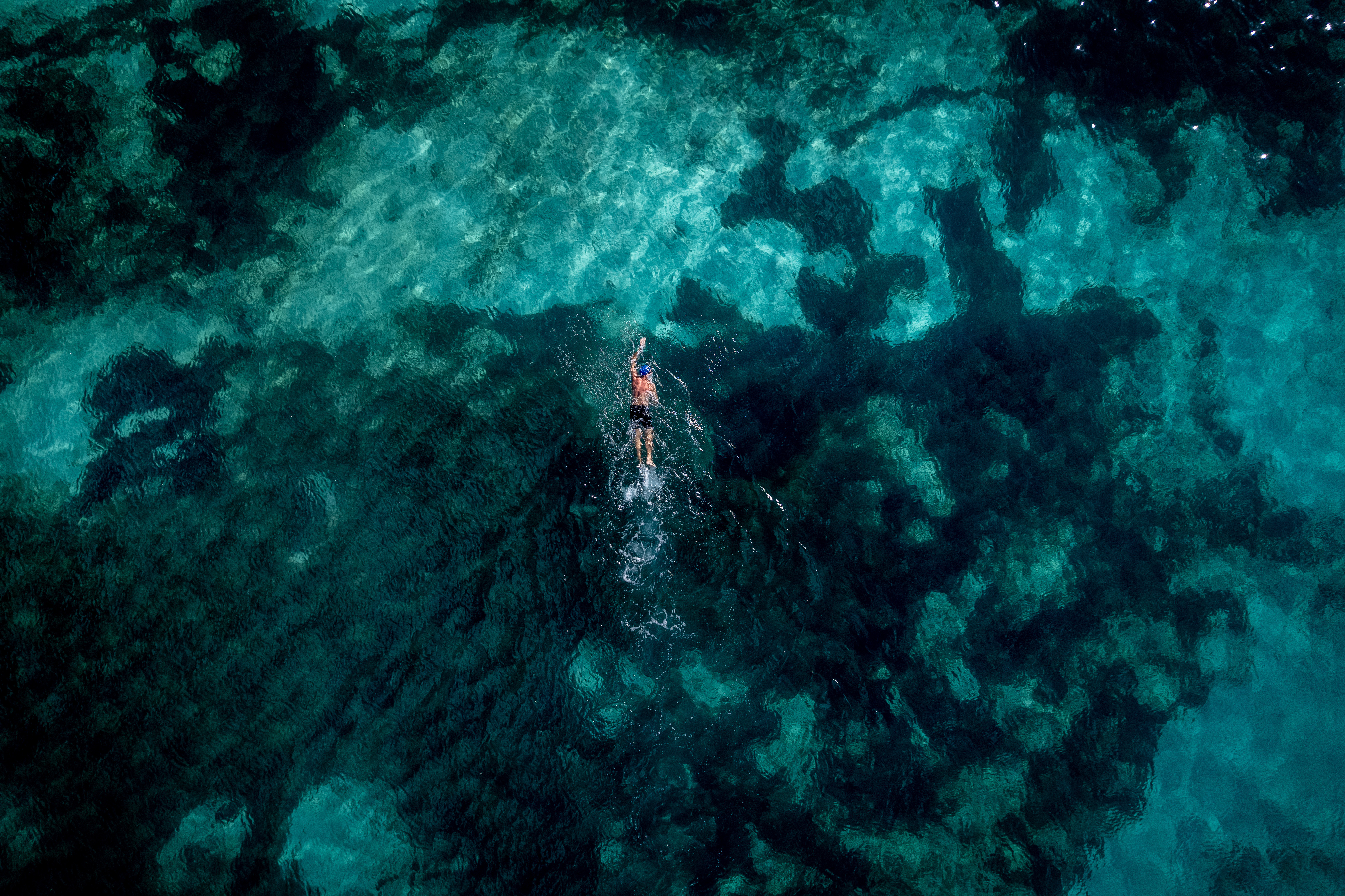 Nadador en aguas turquesas del océano, vista aérea de fondo marino.