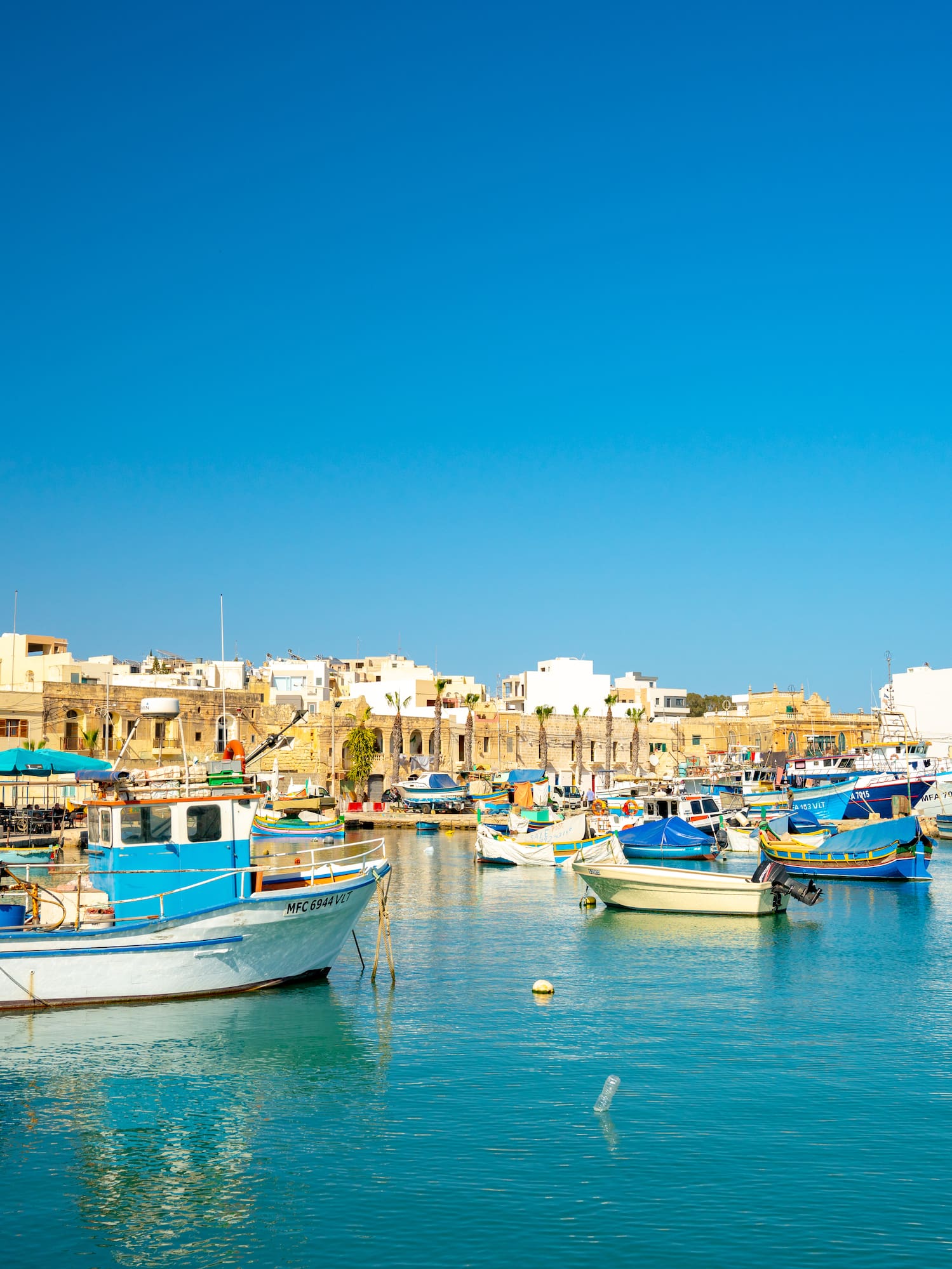 Marsaxlokk harbor, Malta, with traditional Luzzu fishing boats and a Maltese flag.