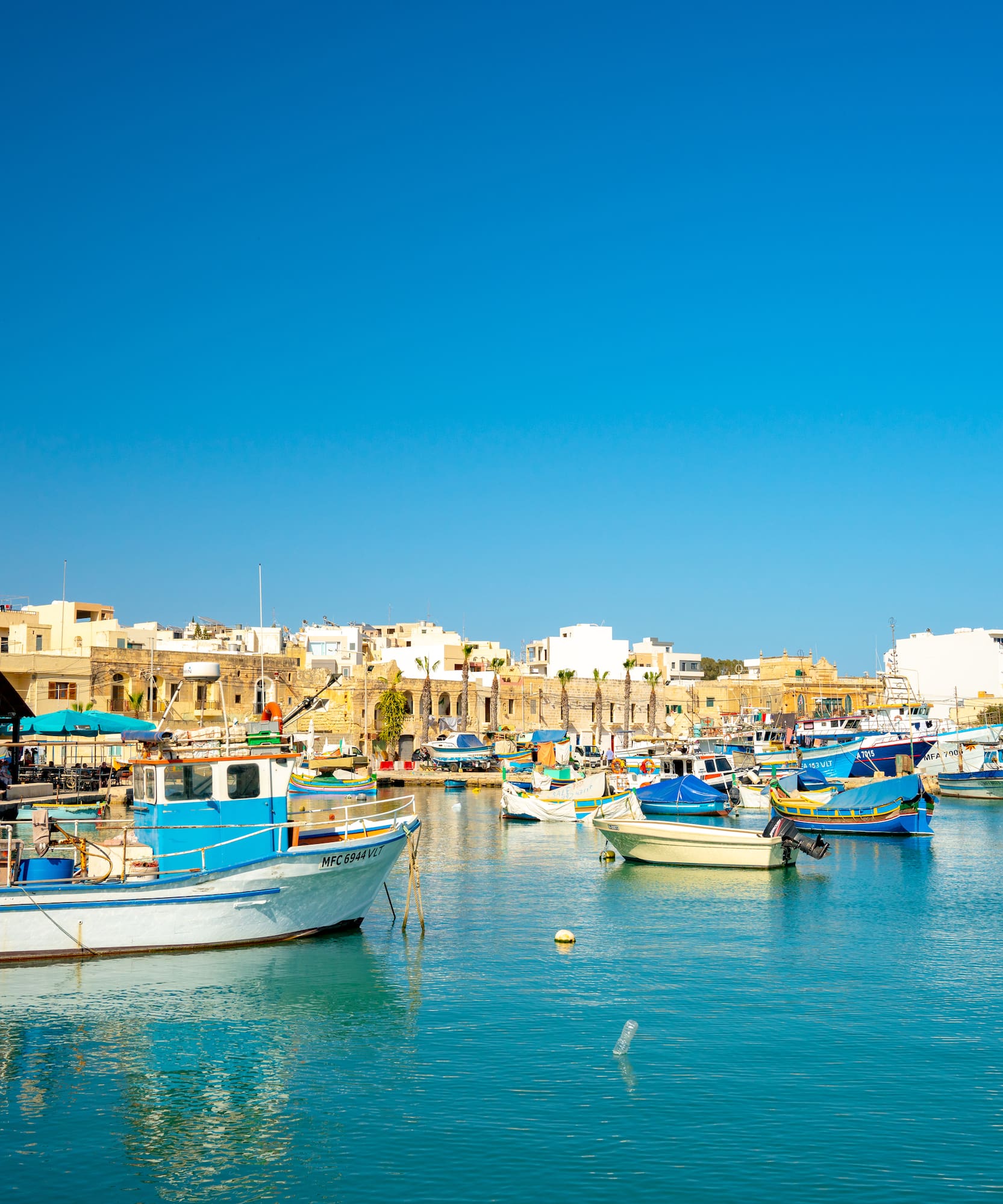 Marsaxlokk harbor, Malta, with traditional Luzzu fishing boats and a Maltese flag.