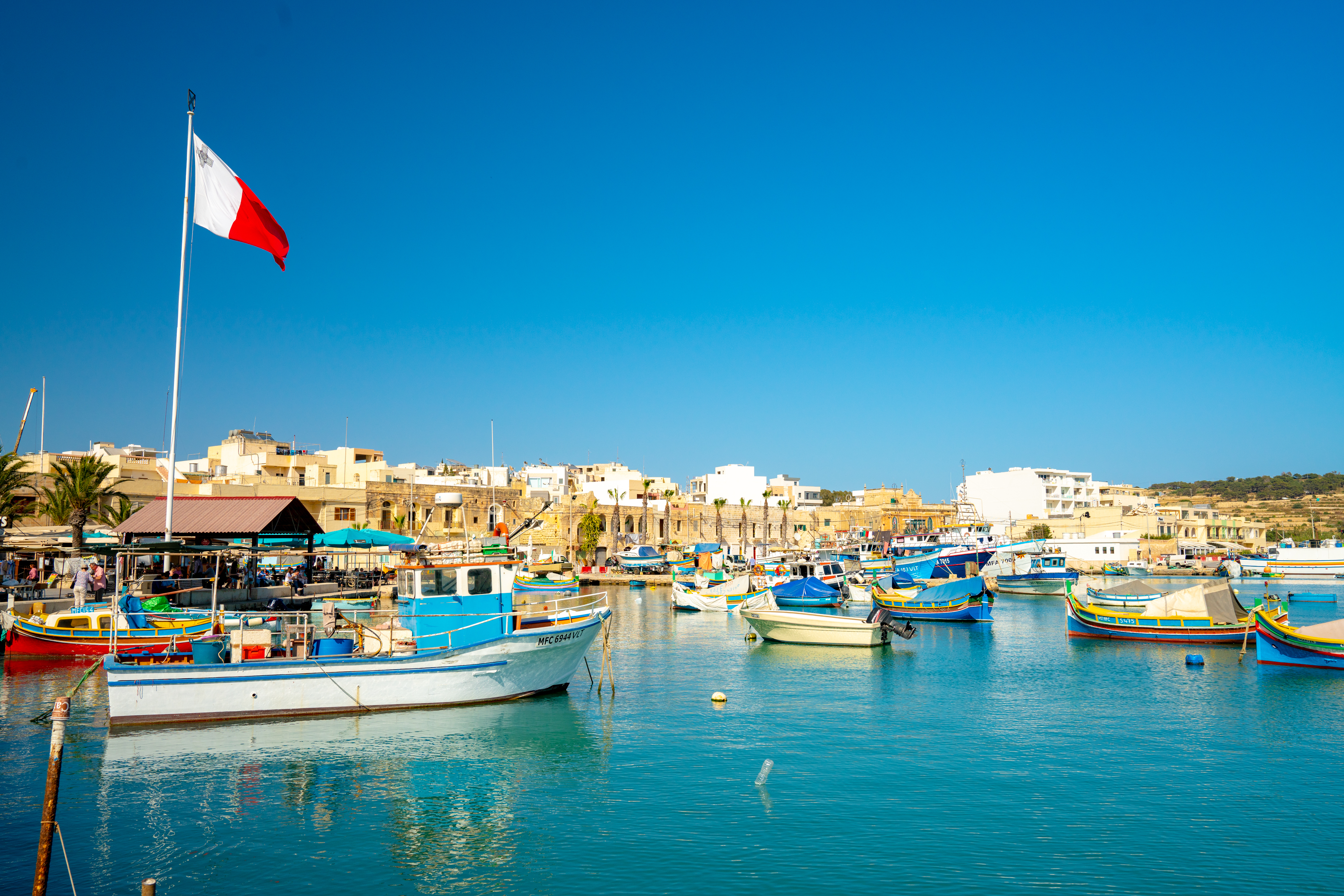 Marsaxlokk harbor, Malta, with traditional Luzzu fishing boats and a Maltese flag.