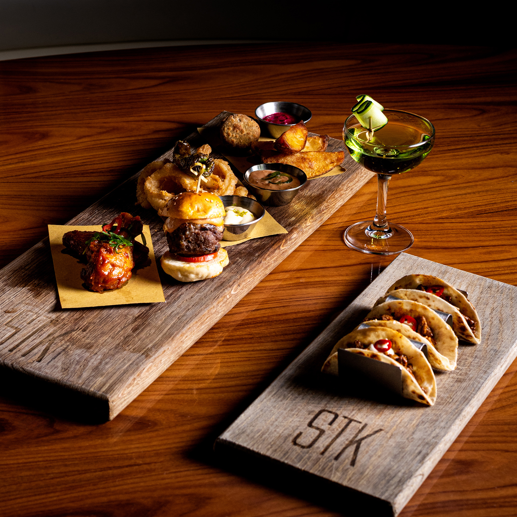 STK appetizer platter: sliders, wings, tacos, fried items, dips, green cocktail.