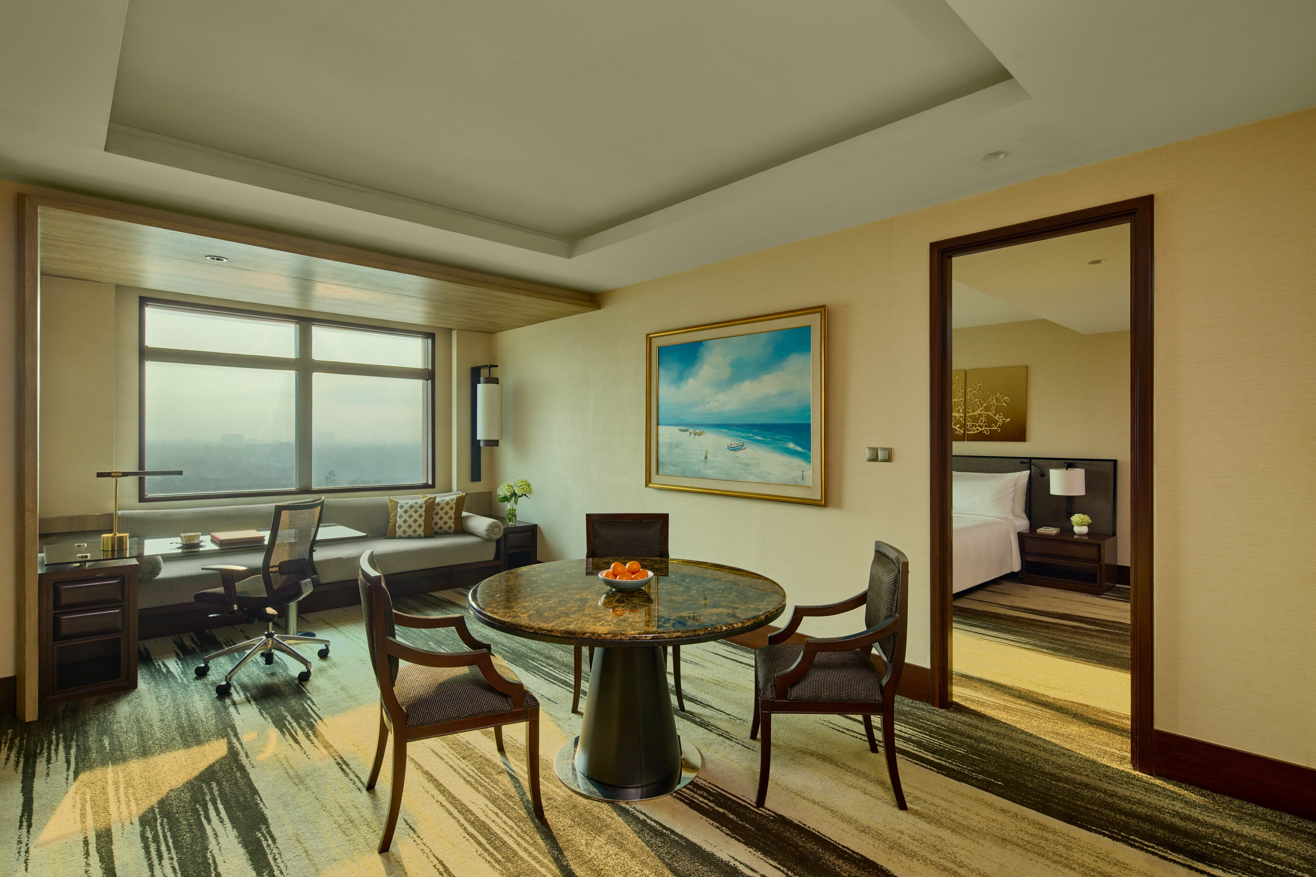 Spacious hotel suite: dining table, work desk by window, bedroom entrance.