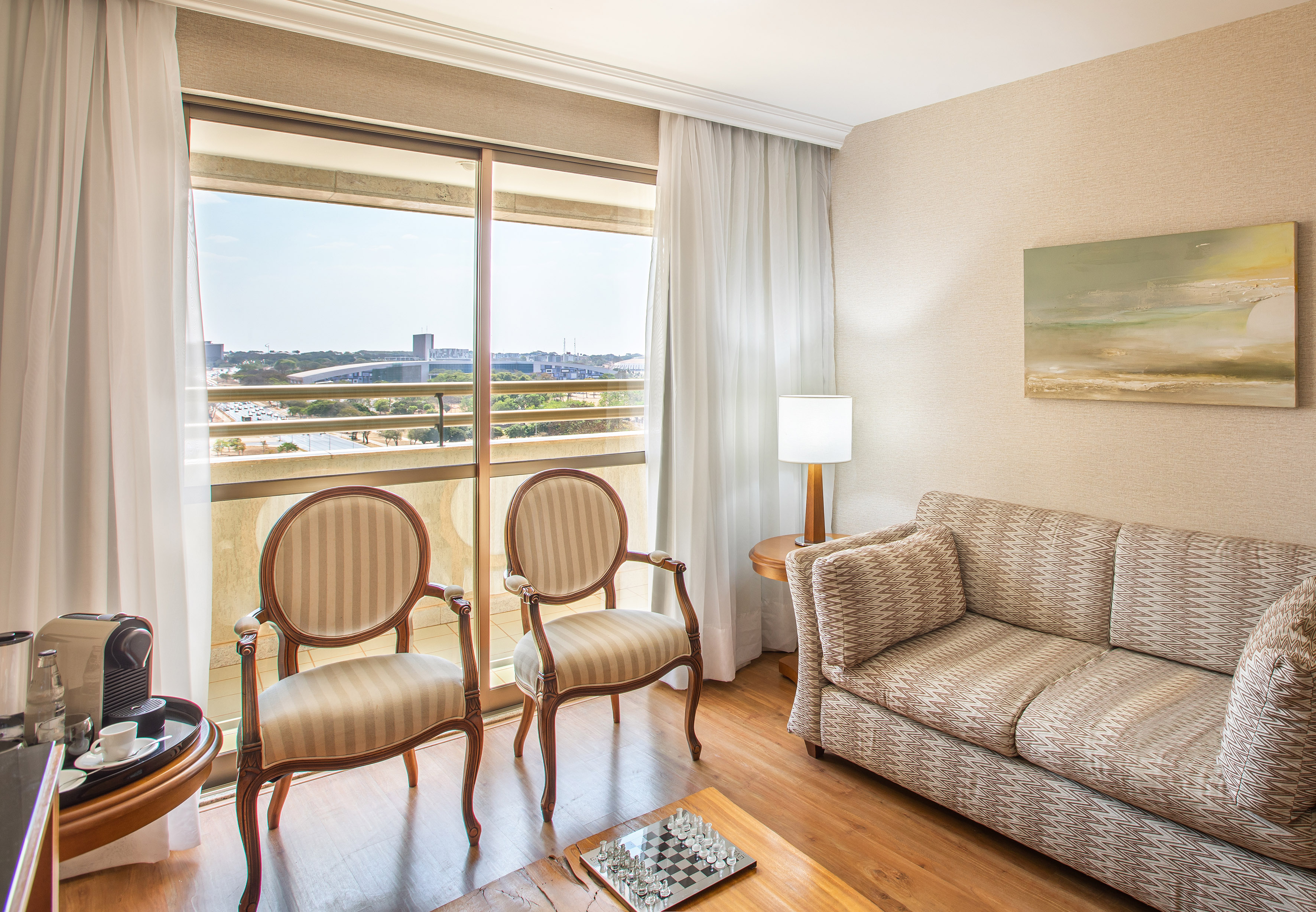 Hotel suite living area with city view, patterned sofa, and elegant armchairs.