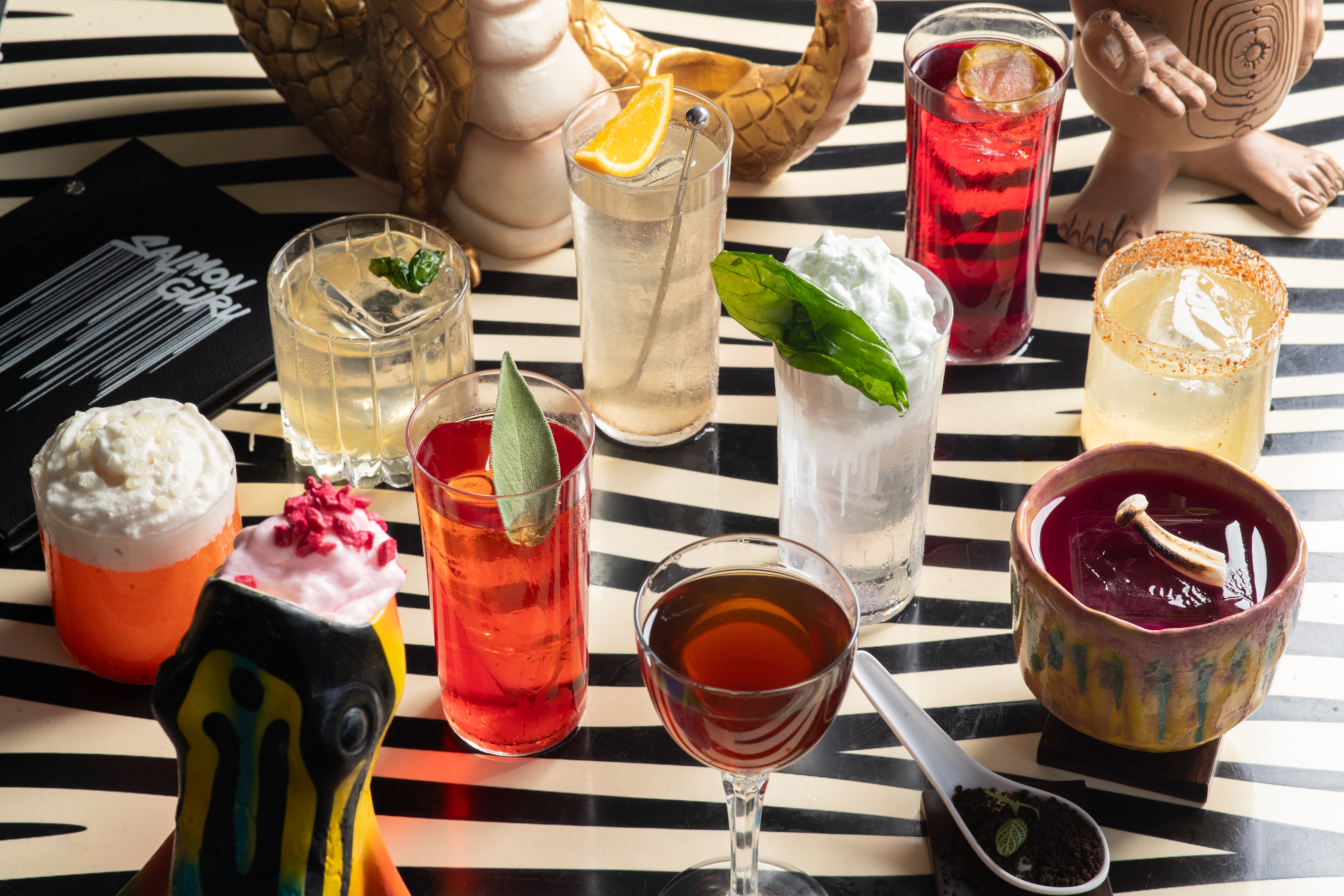Vibrant array of gourmet cocktails with diverse garnishes on striped table.