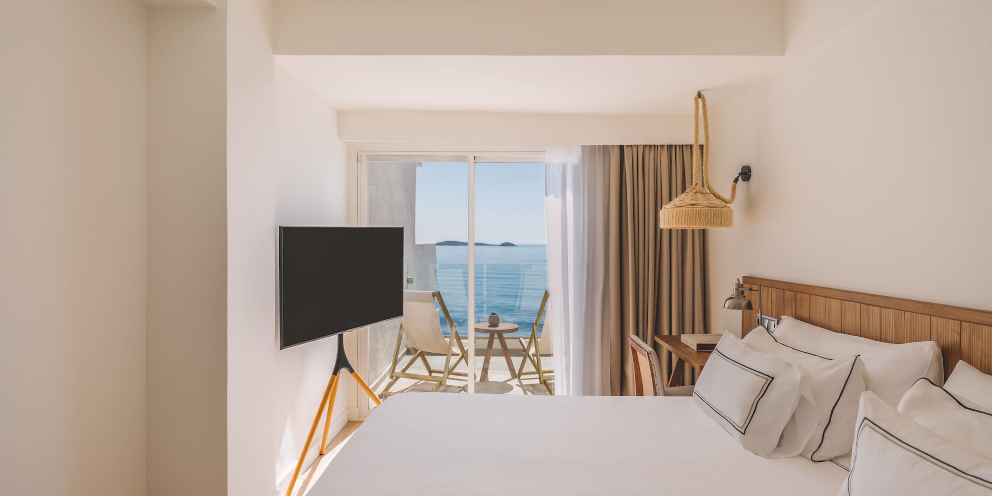 Bright modern hotel room with ocean view balcony and white bed.