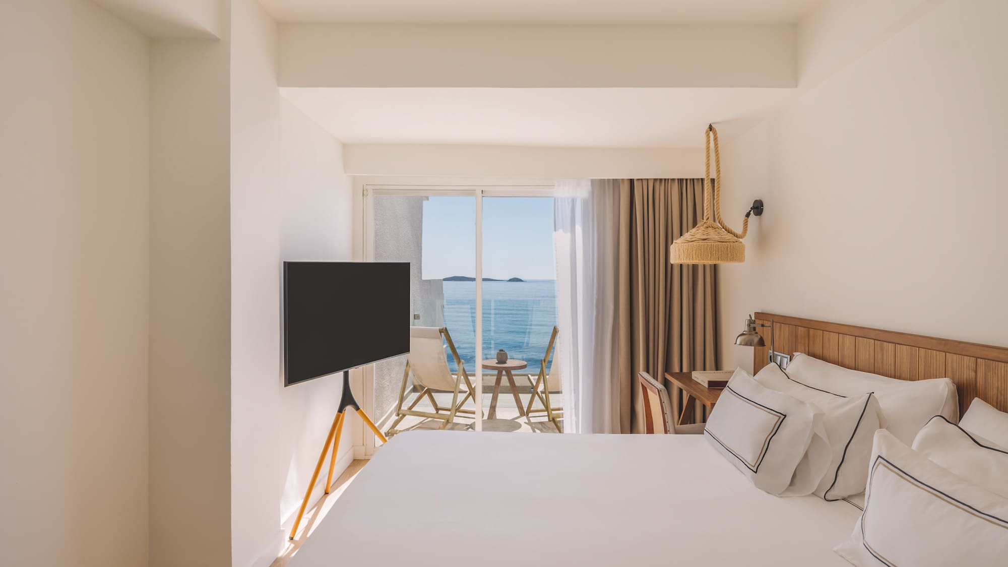 Bright modern hotel room with ocean view balcony and white bed.
