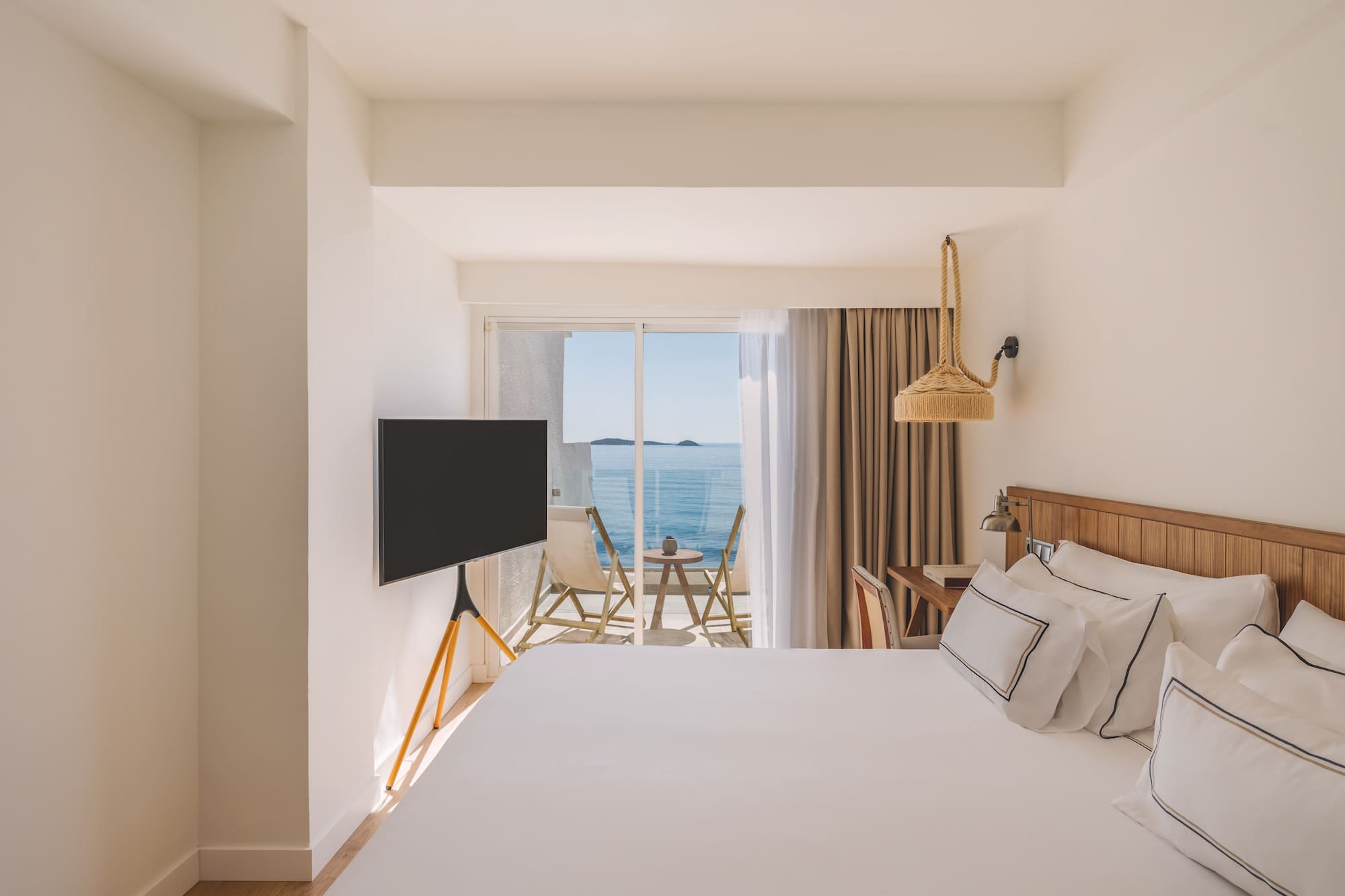 Bright modern hotel room with ocean view balcony and white bed.