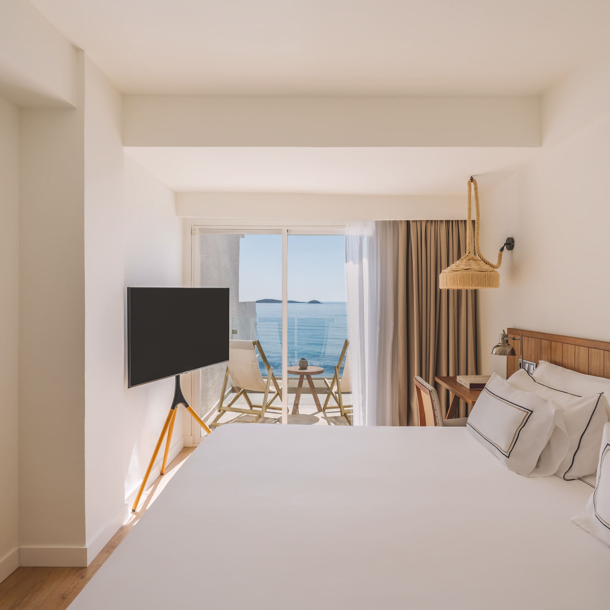 Bright modern hotel room with ocean view balcony and white bed.