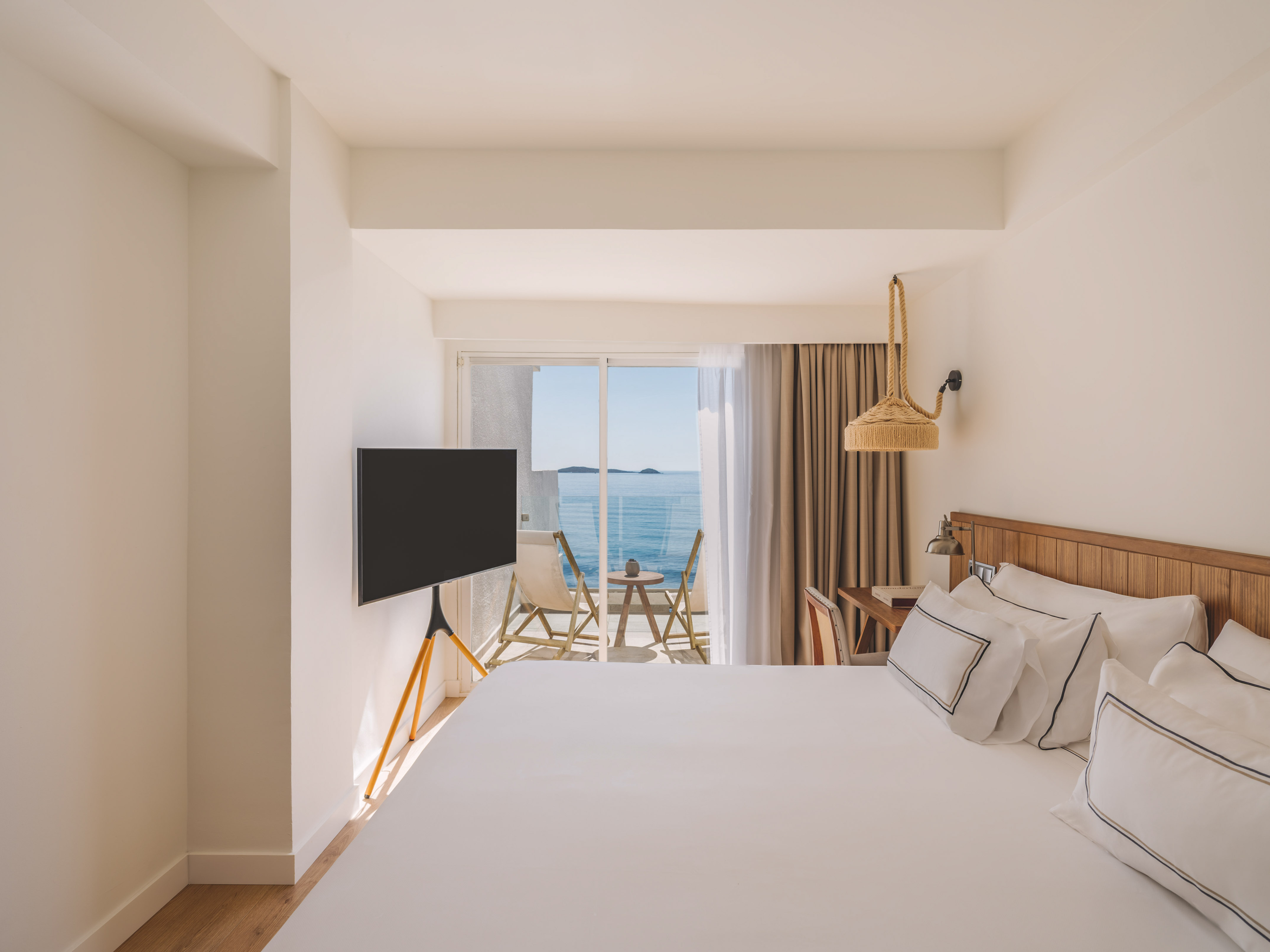 Bright modern hotel room with ocean view balcony and white bed.