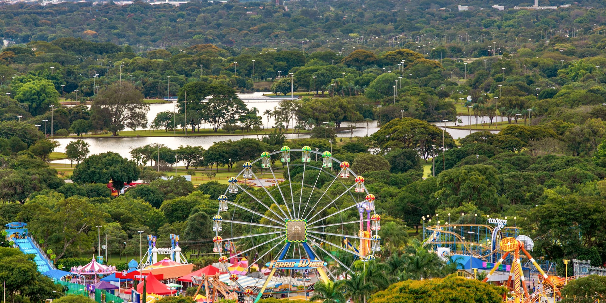 Amusement park with Ferris wheel and rides in a green urban park, city beyond.