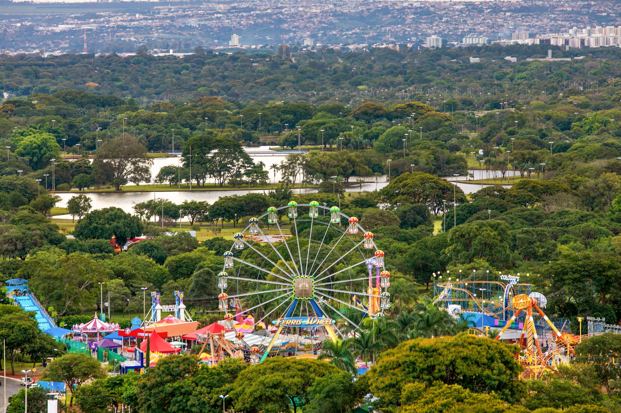 Amusement park with Ferris wheel and rides in a green urban park, city beyond.