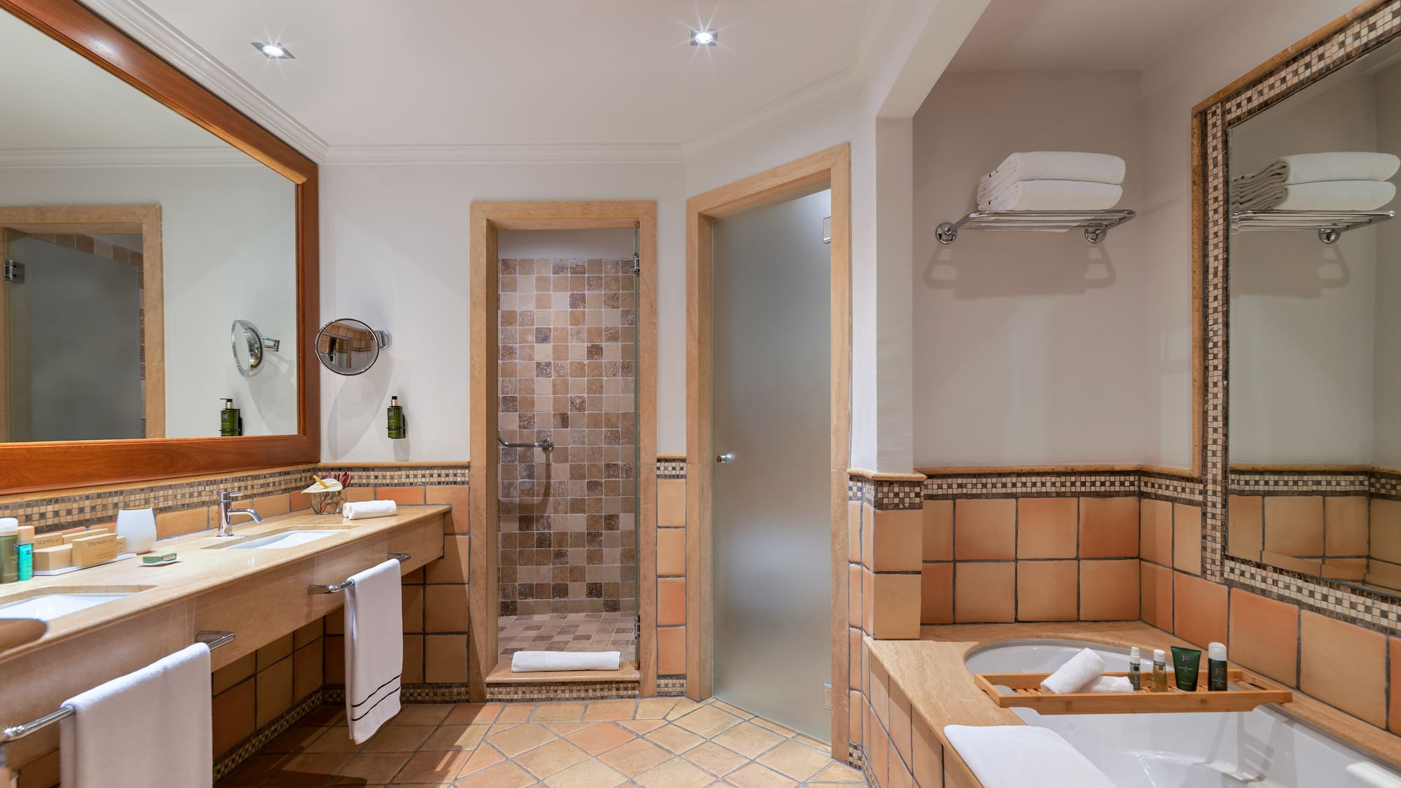 Terracotta tiled bathroom with double vanity, walk-in shower, and bathtub.