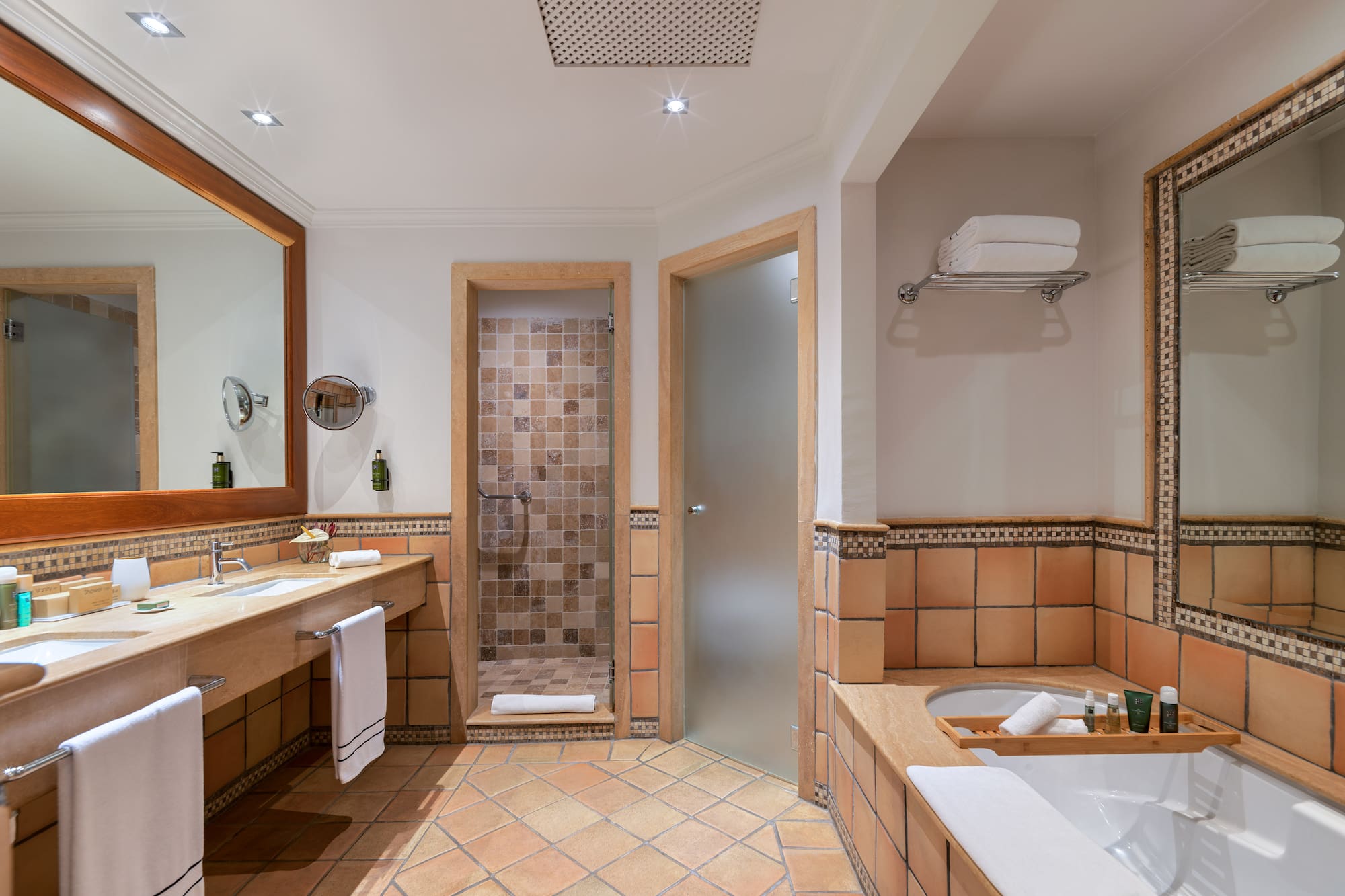 Terracotta tiled bathroom with double vanity, walk-in shower, and bathtub.