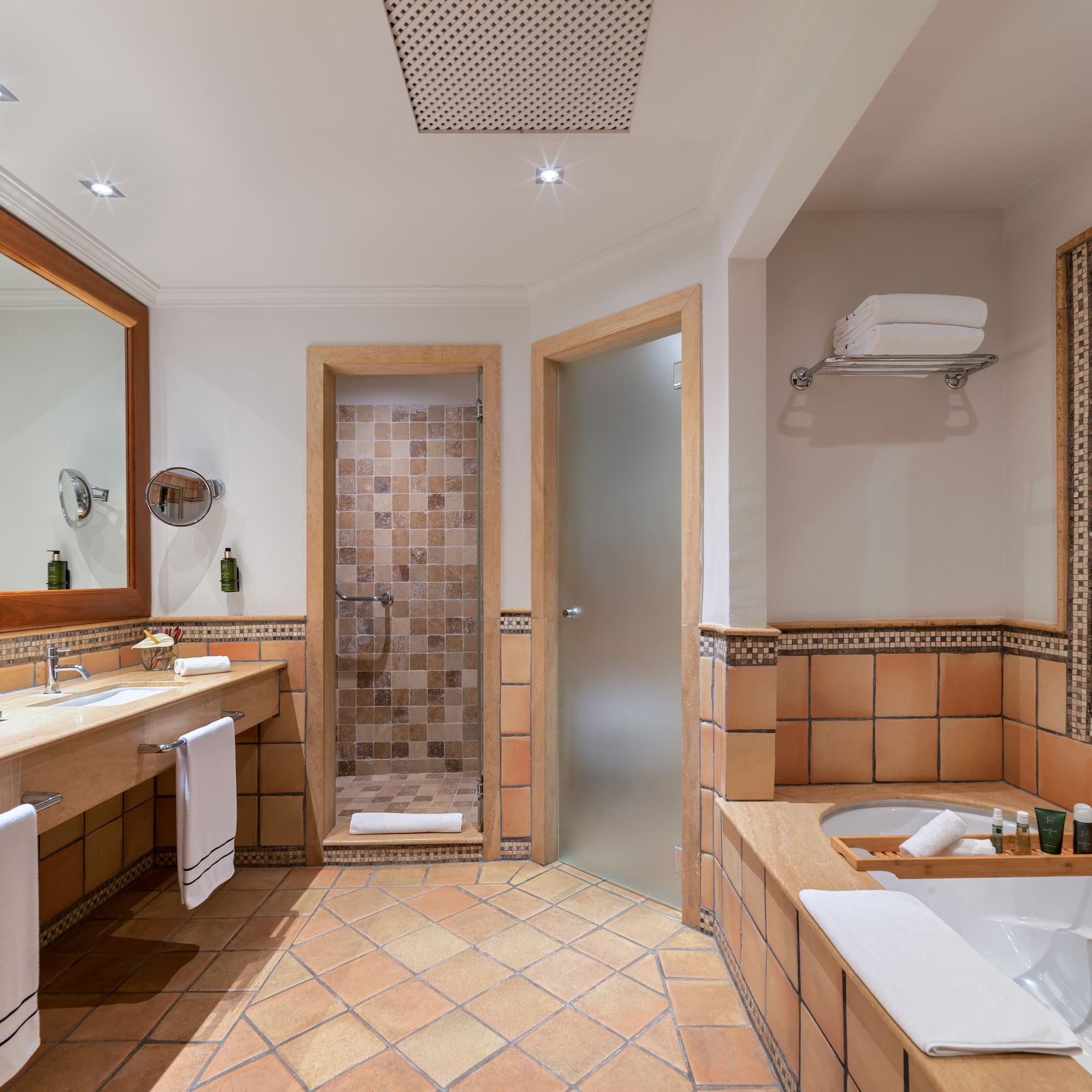 Terracotta tiled bathroom with double vanity, walk-in shower, and bathtub.