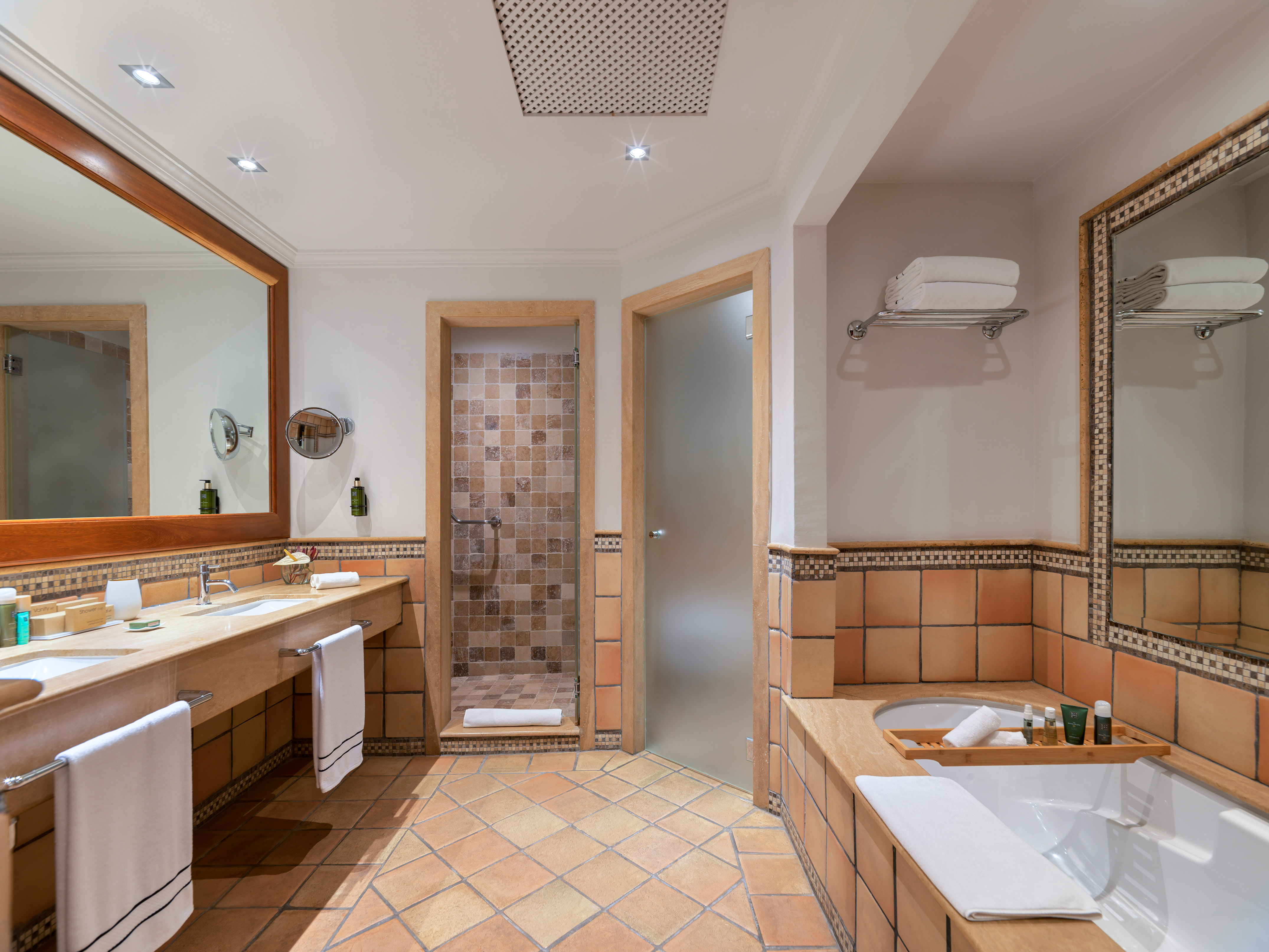Terracotta tiled bathroom with double vanity, walk-in shower, and bathtub.