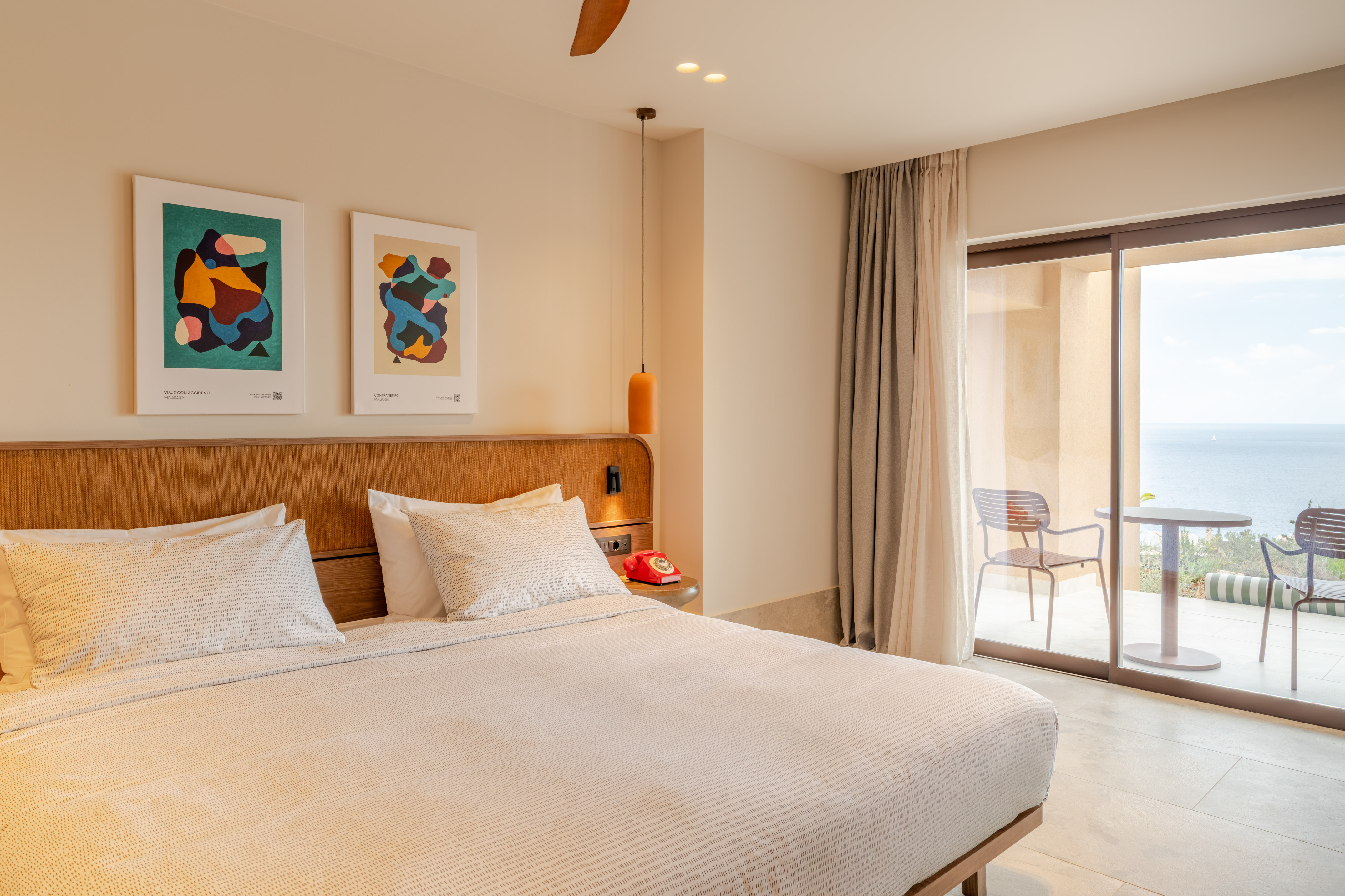 Modern hotel bedroom with ocean view, abstract art, and balcony.
