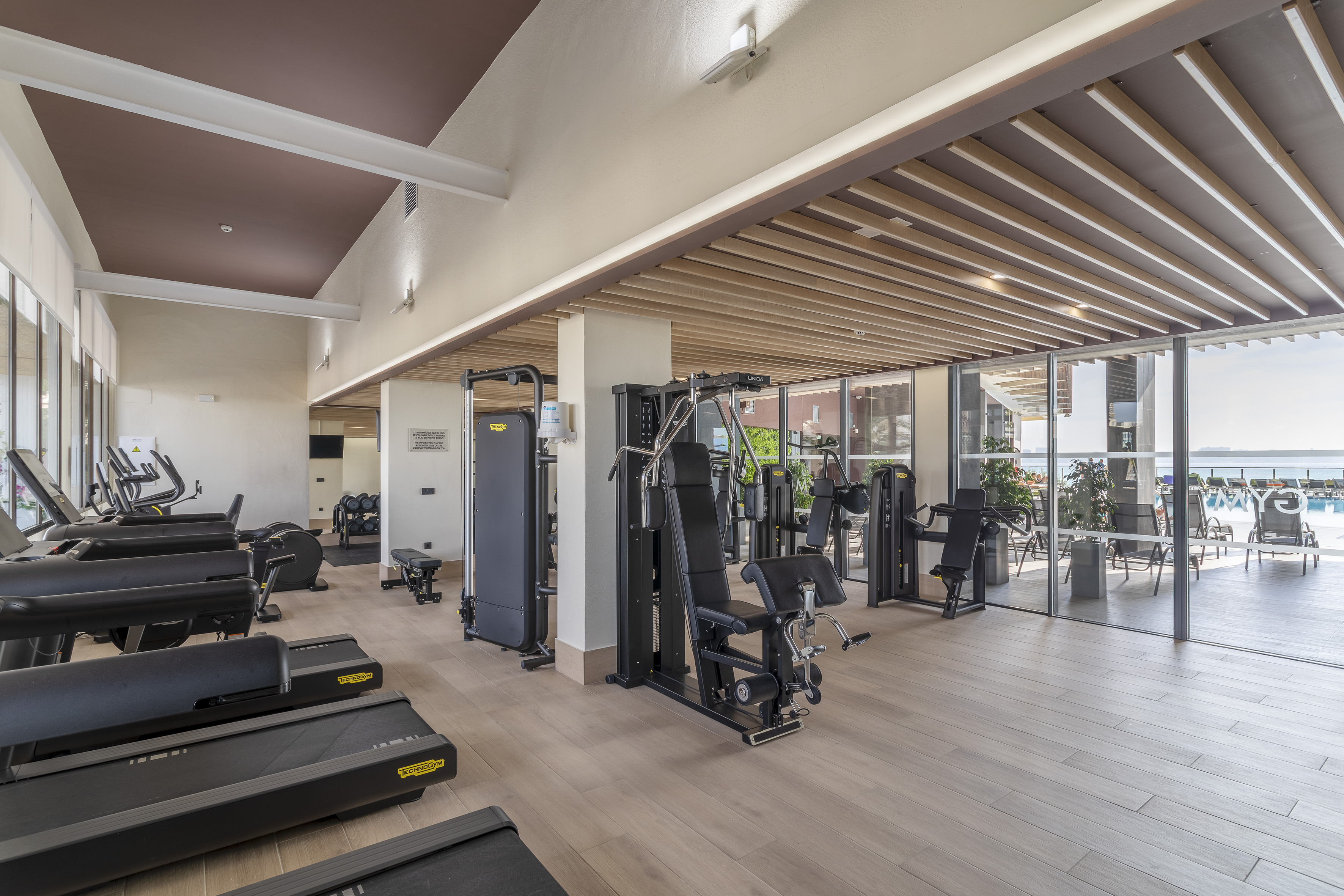 Modern fitness center with exercise equipment and ocean view through large windows.